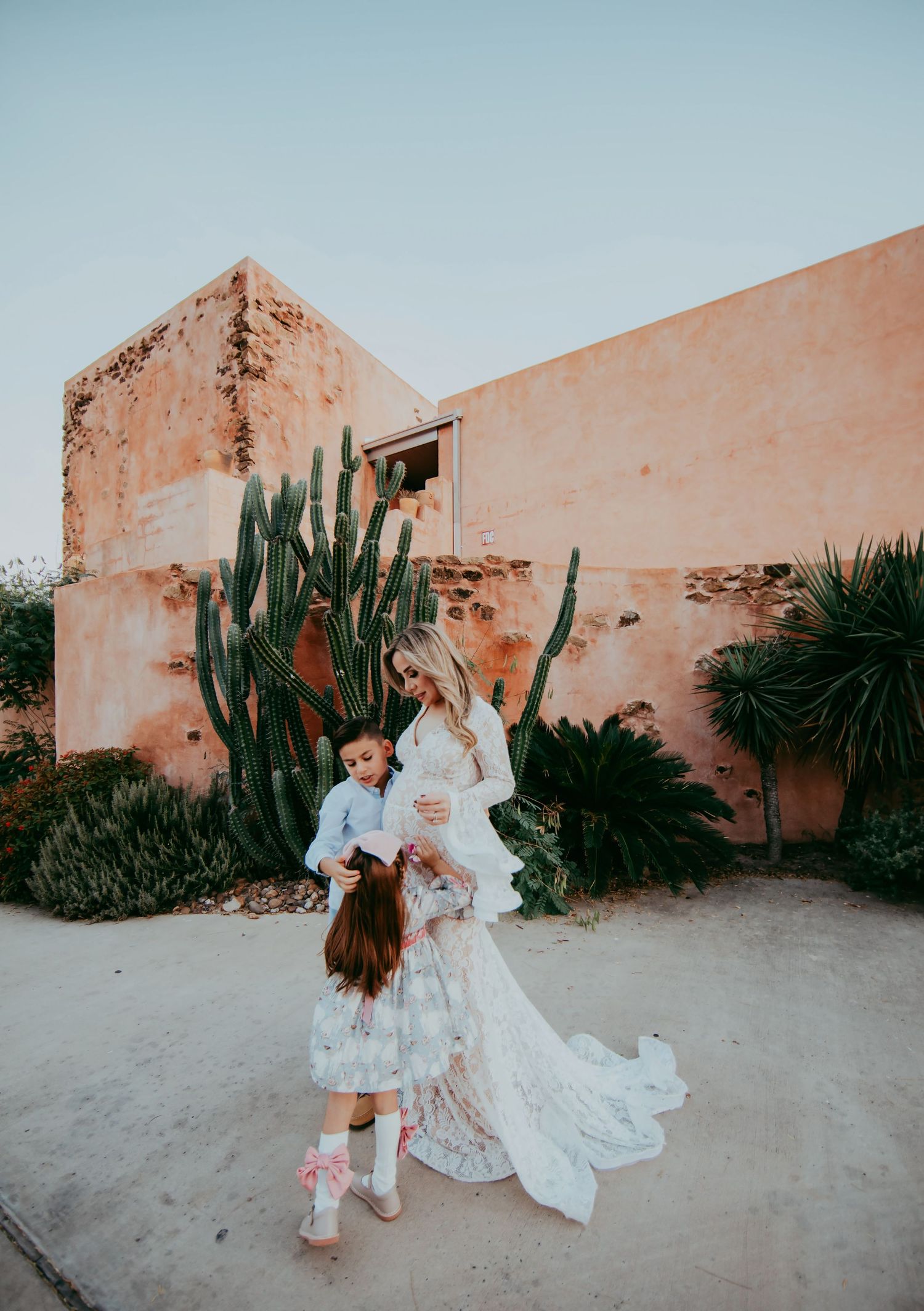 A sweet moment between mother and child against a rustic pink wall with cacti.
