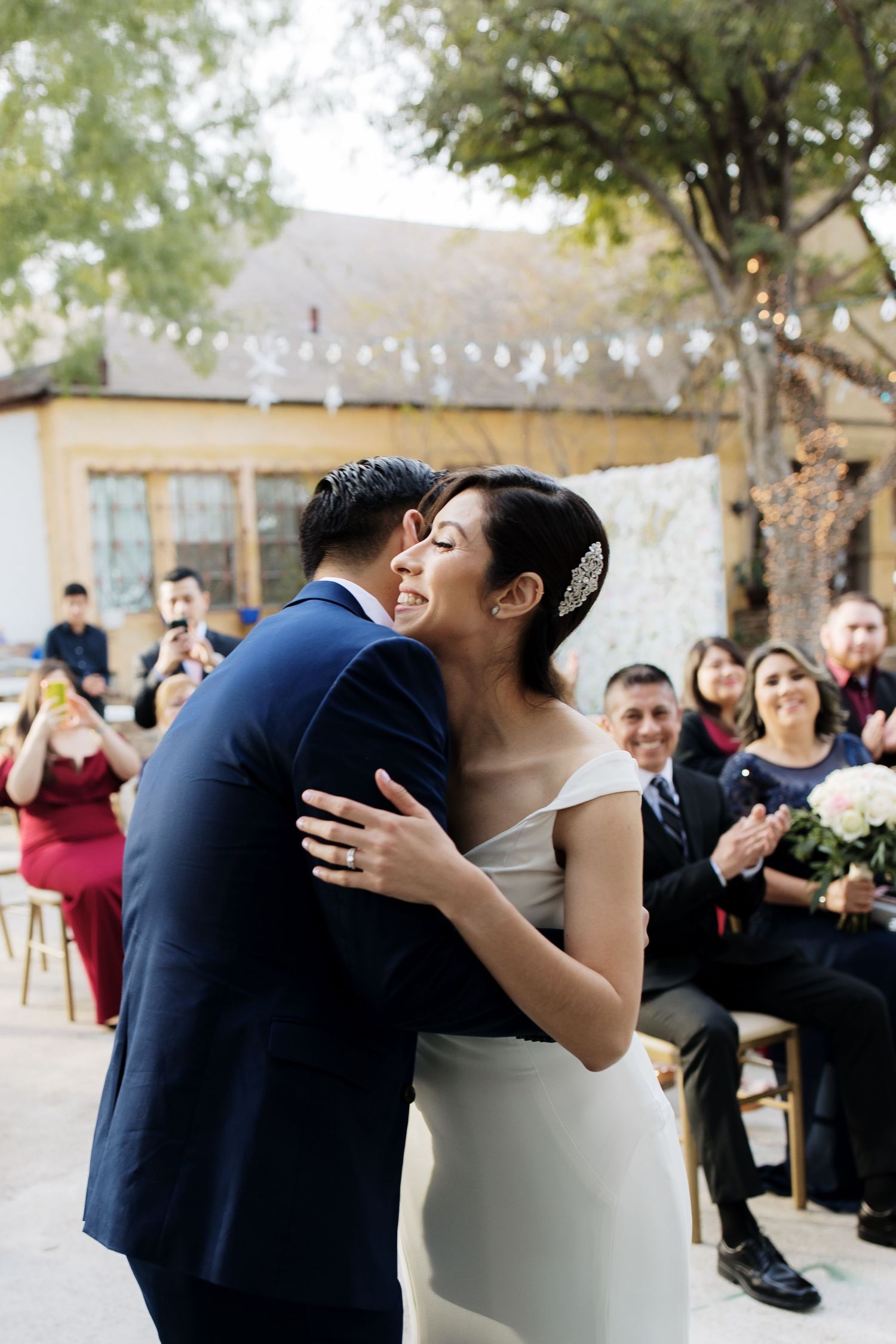Bride and groom share a joyful embrace during their outdoor wedding ceremony as guests applaud.