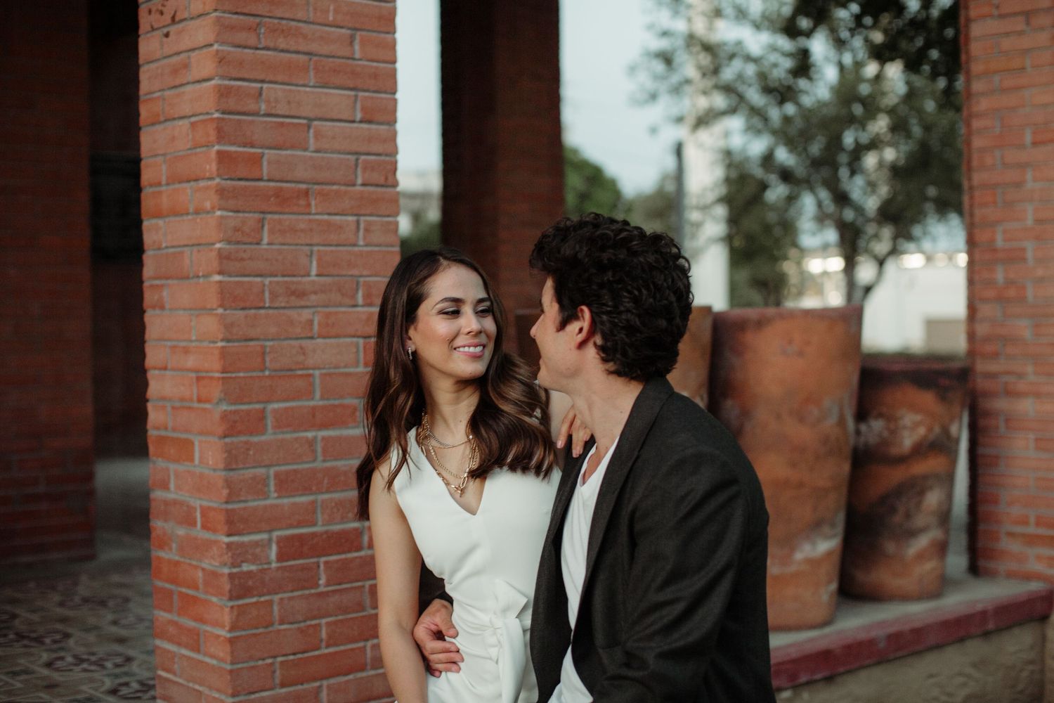 Couple smiling at each other near brick columns during an engagement photo session.