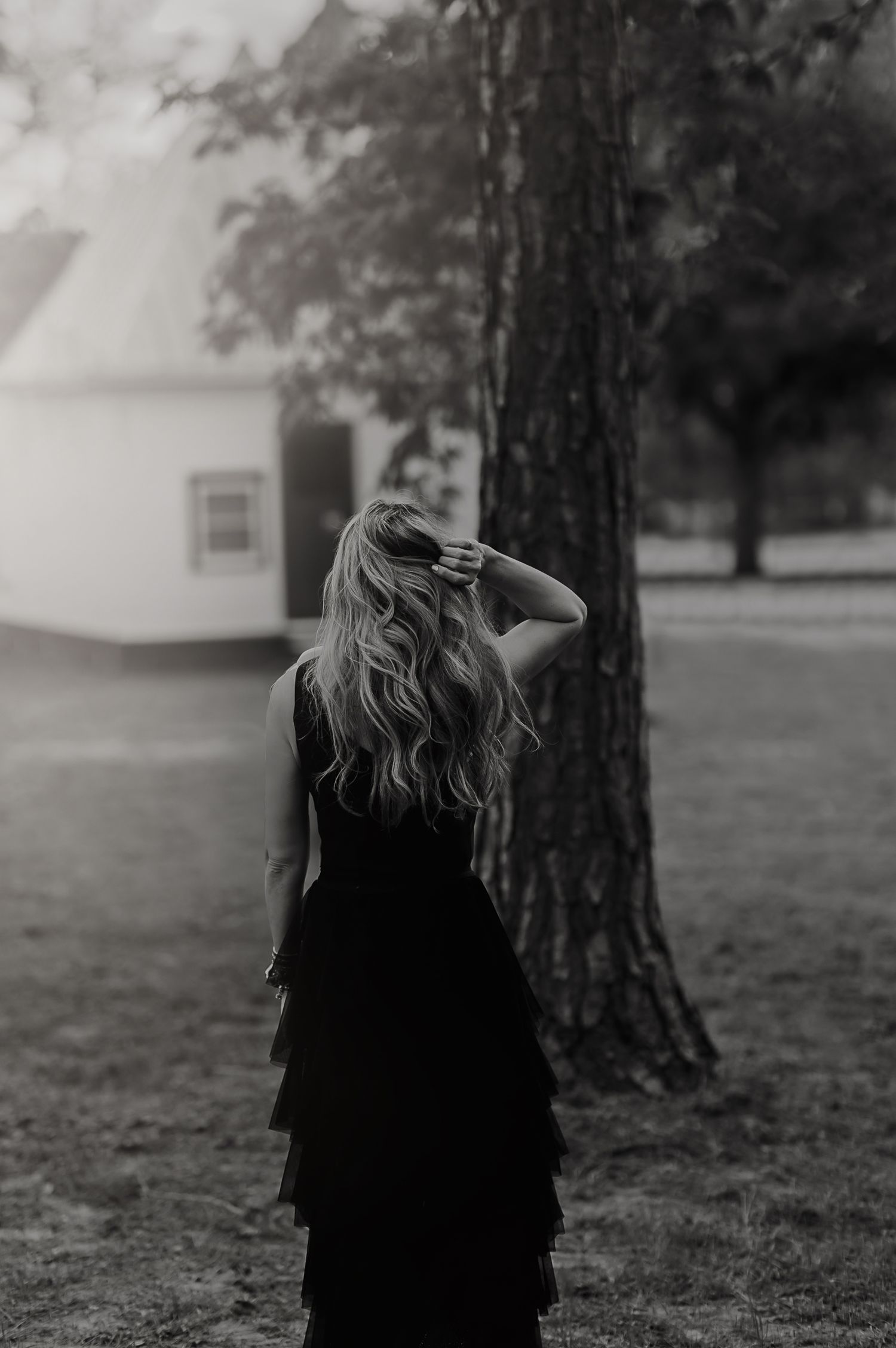 Atmospheric black and white photo of a person in a black dress standing near a tree in a misty setting.