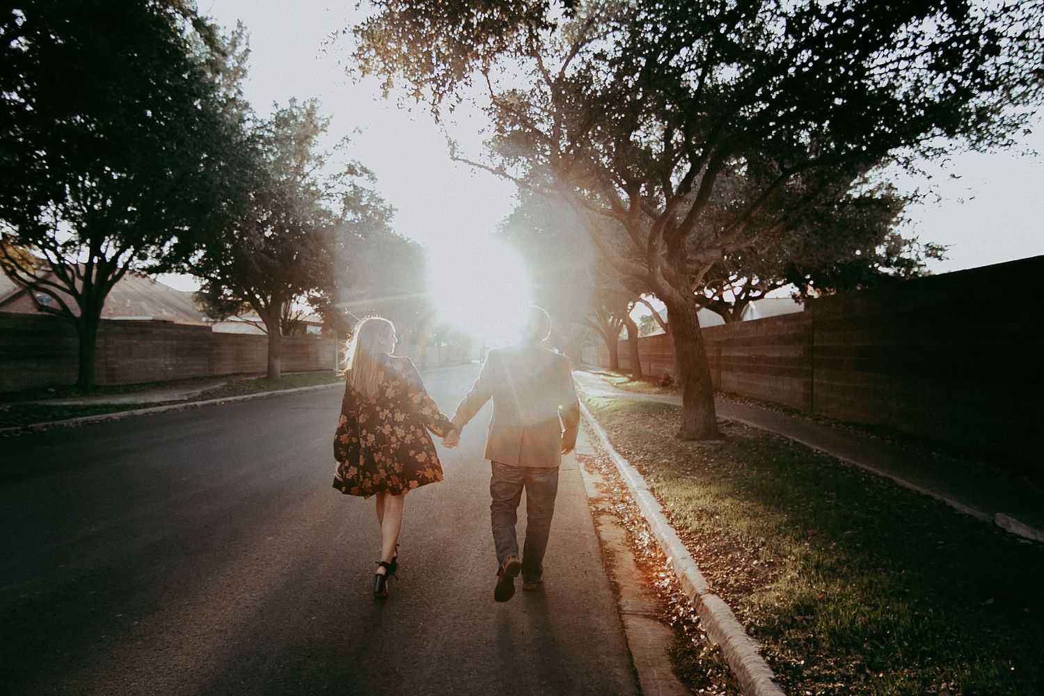 A couple walks hand in hand down a sunlit tree-lined street during golden hour.