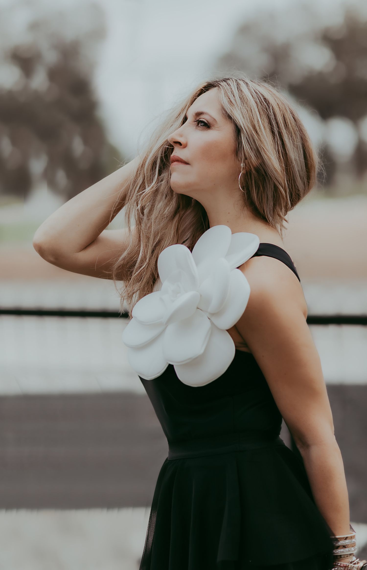 Artistic portrait of woman in black dress with large white flower accent looking up dramatically.