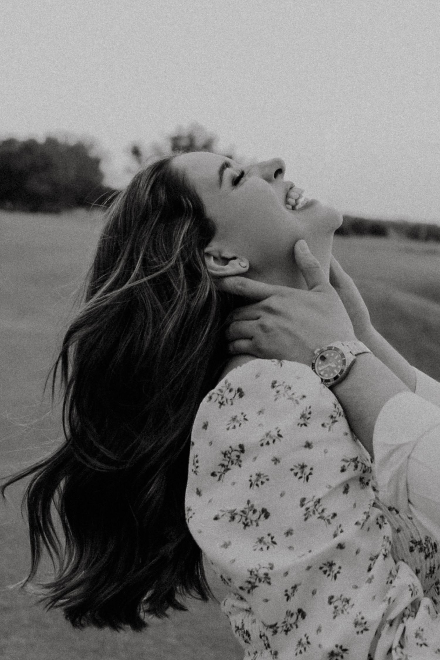 Black and white photo of a laughing woman with long dark hair being embraced outdoors.