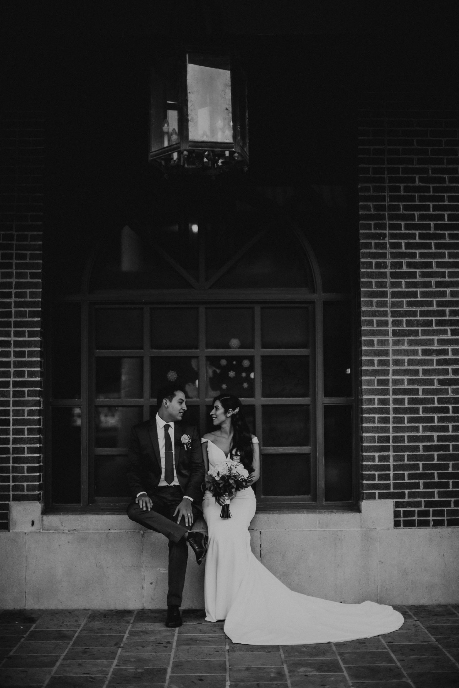 Black and white photo of bride and groom sharing an intimate moment outside a brick building at night.