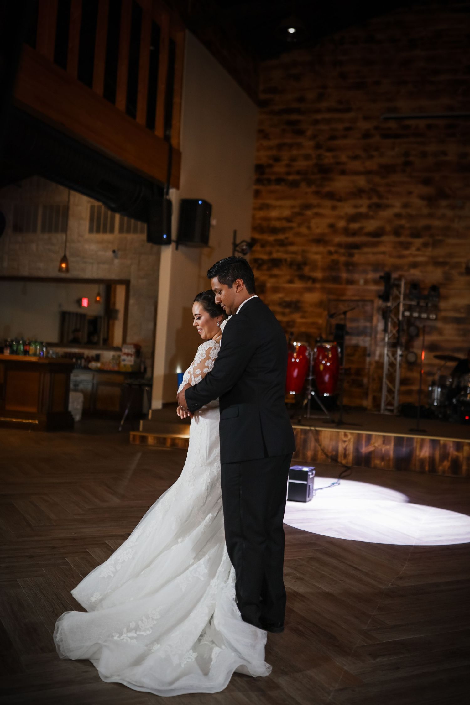 Bride and groom share intimate first dance in rustic wedding venue with exposed brick wall.