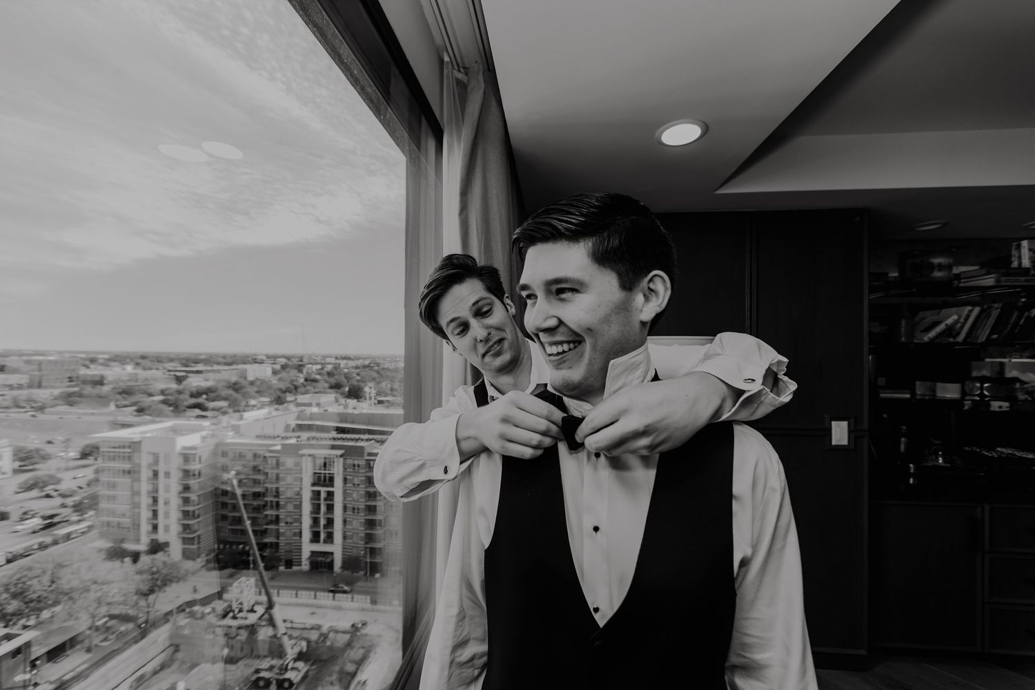 Black and white candid moment of two people embracing by a high-rise window.