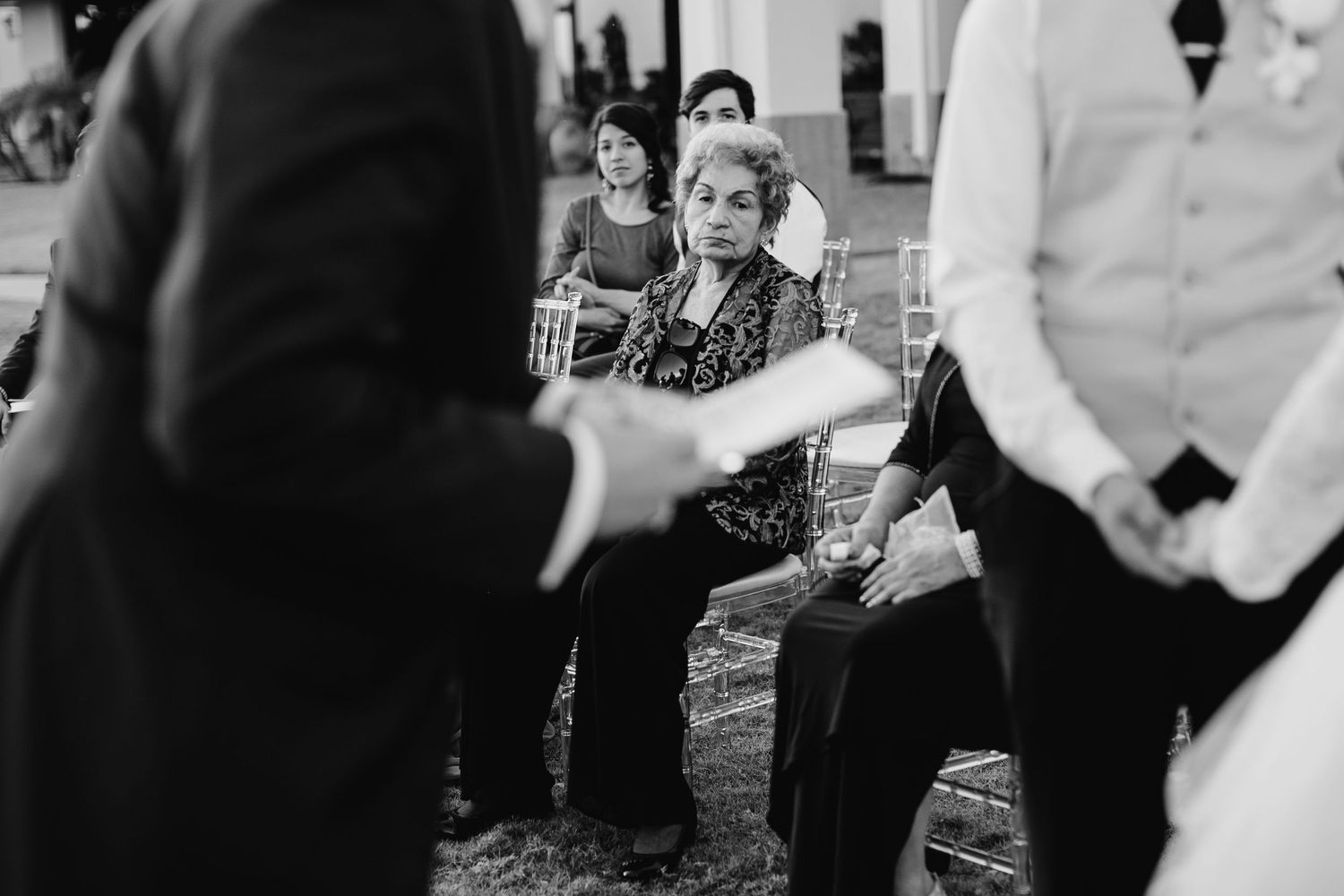 Black and white candid photo of wedding guests seated during an outdoor wedding ceremony.