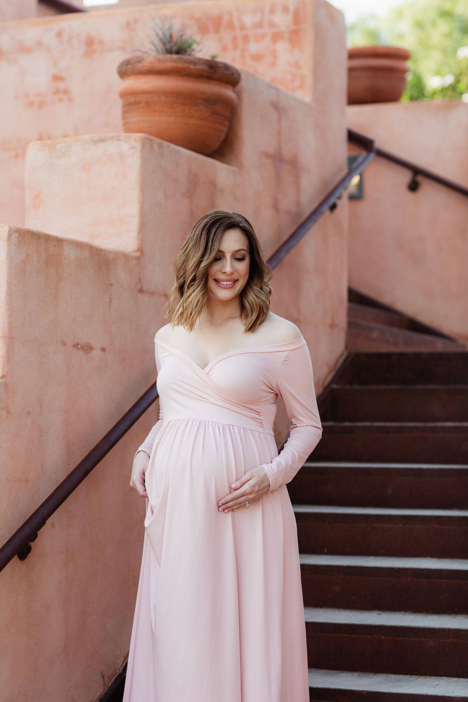 Romantic maternity portrait on terracotta steps with potted plants and warm desert architecture.