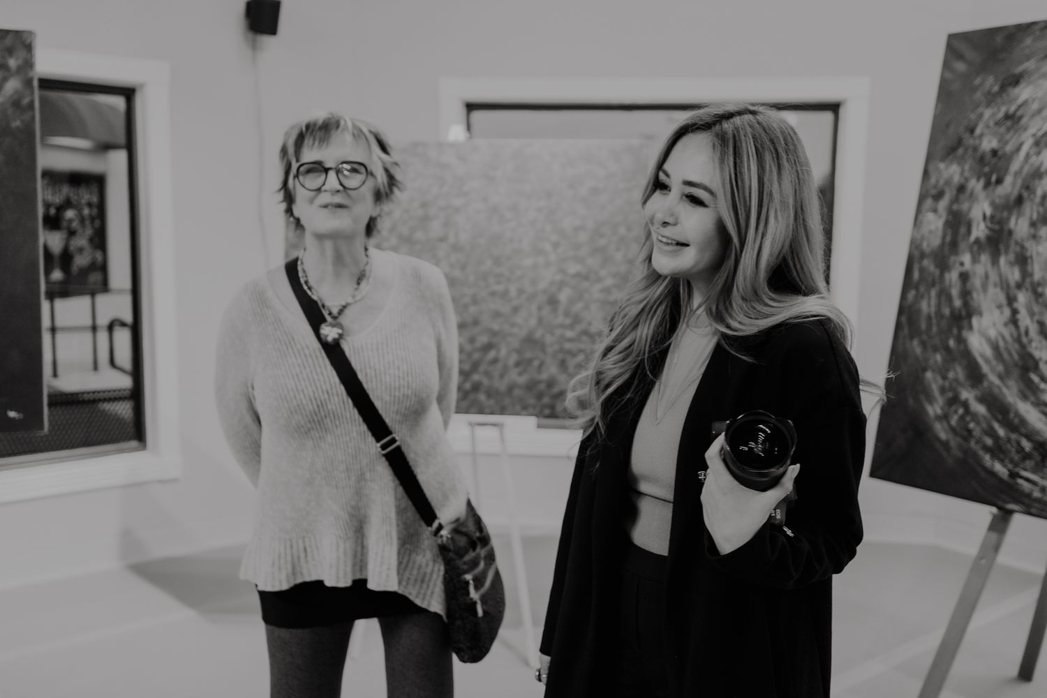 Two people smile and interact while viewing artwork in a gallery exhibition space. photography classes, photo mentorship, education.
