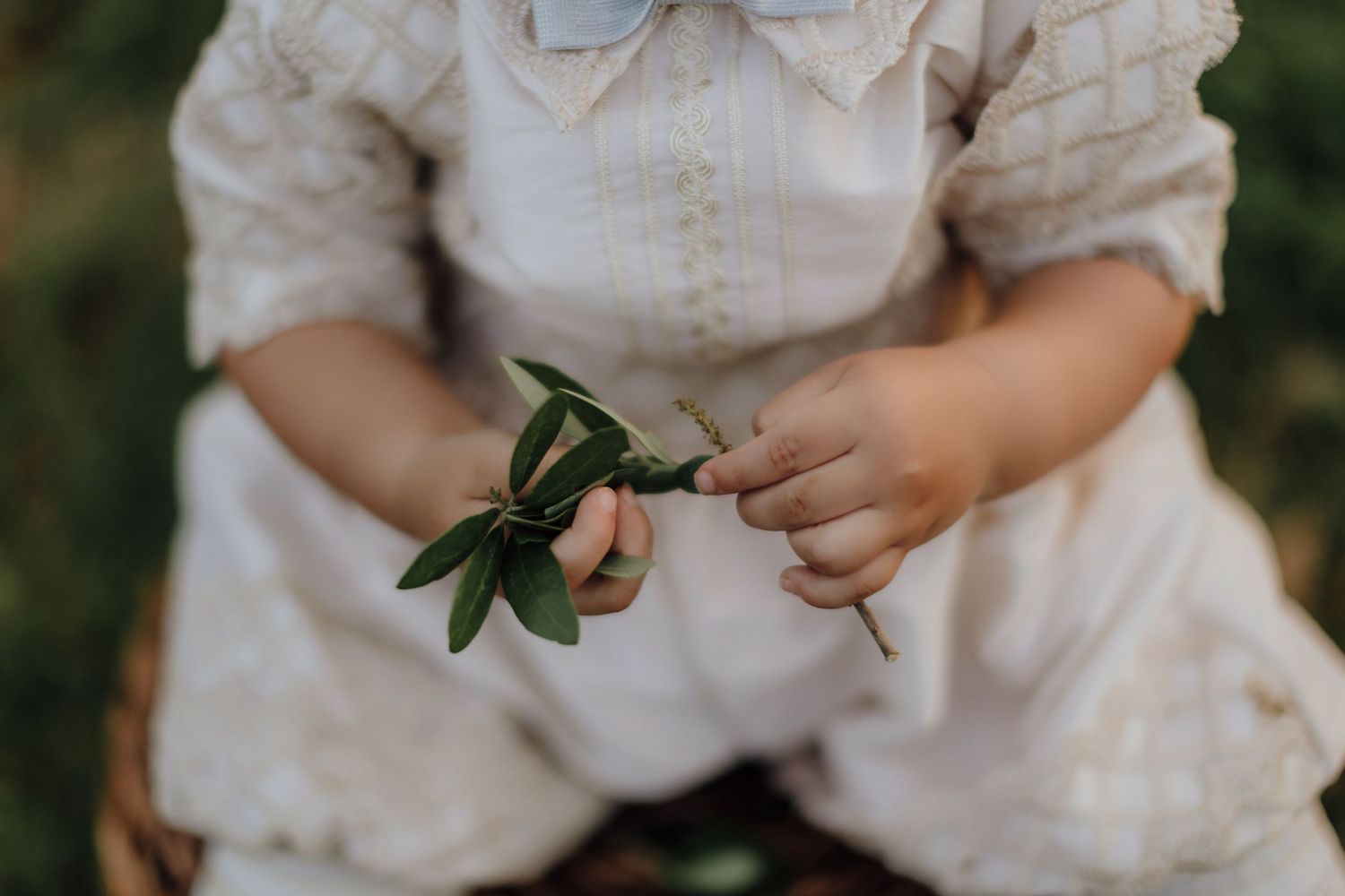Small hands in vintage clothing hold green leaves delicately.