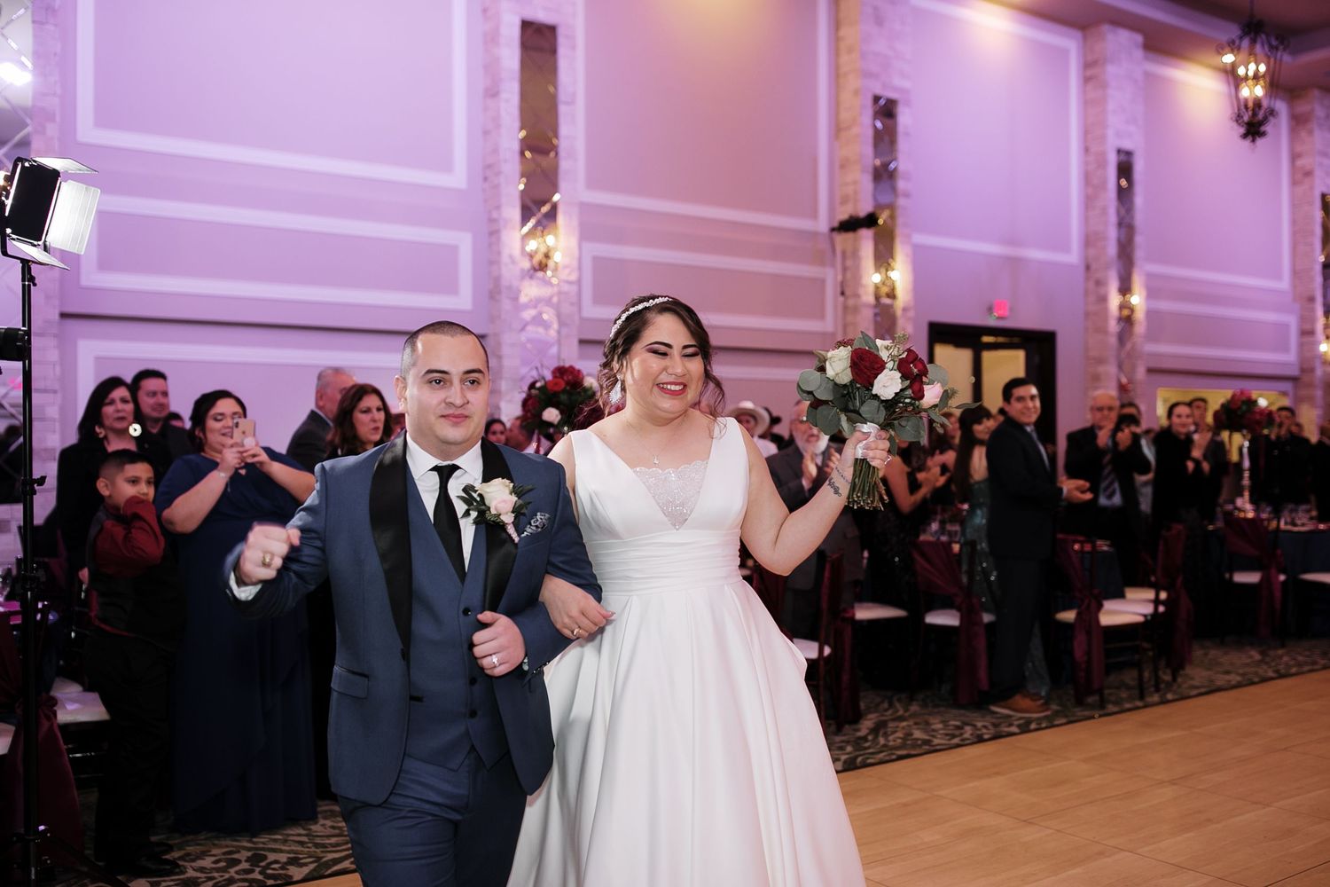 Joyful bride and groom walk triumphantly through reception hall as guests celebrate their marriage.