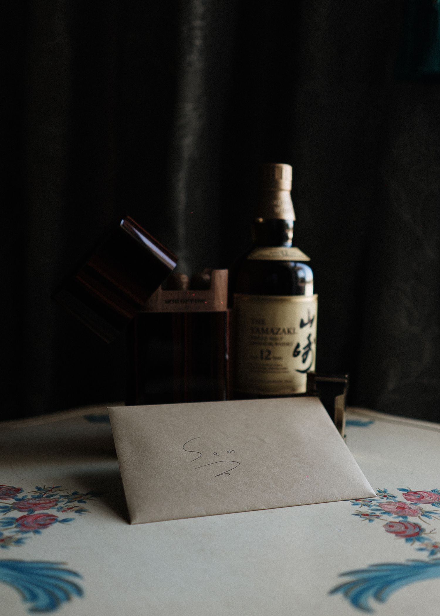 Suntory Yamazaki 12 year Japanese whisky bottle displayed with wooden box and kraft paper gift envelope on floral tablecloth.