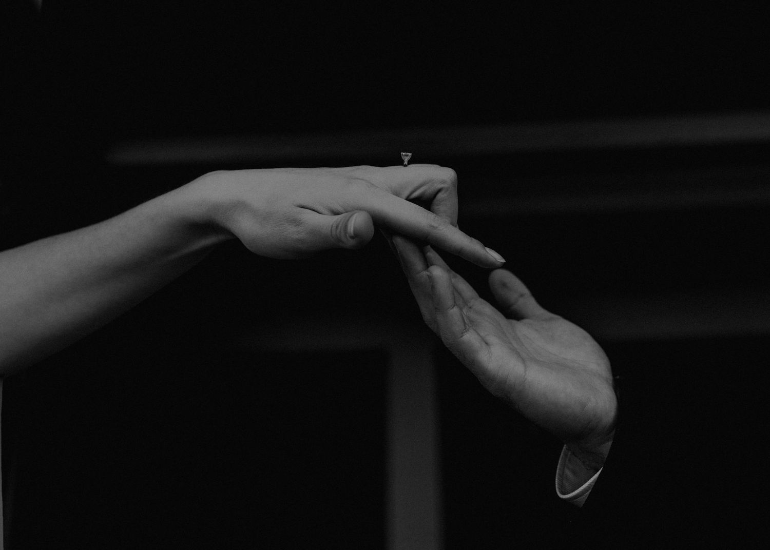 Black and white photo of two hands touching fingertips against a dark background.