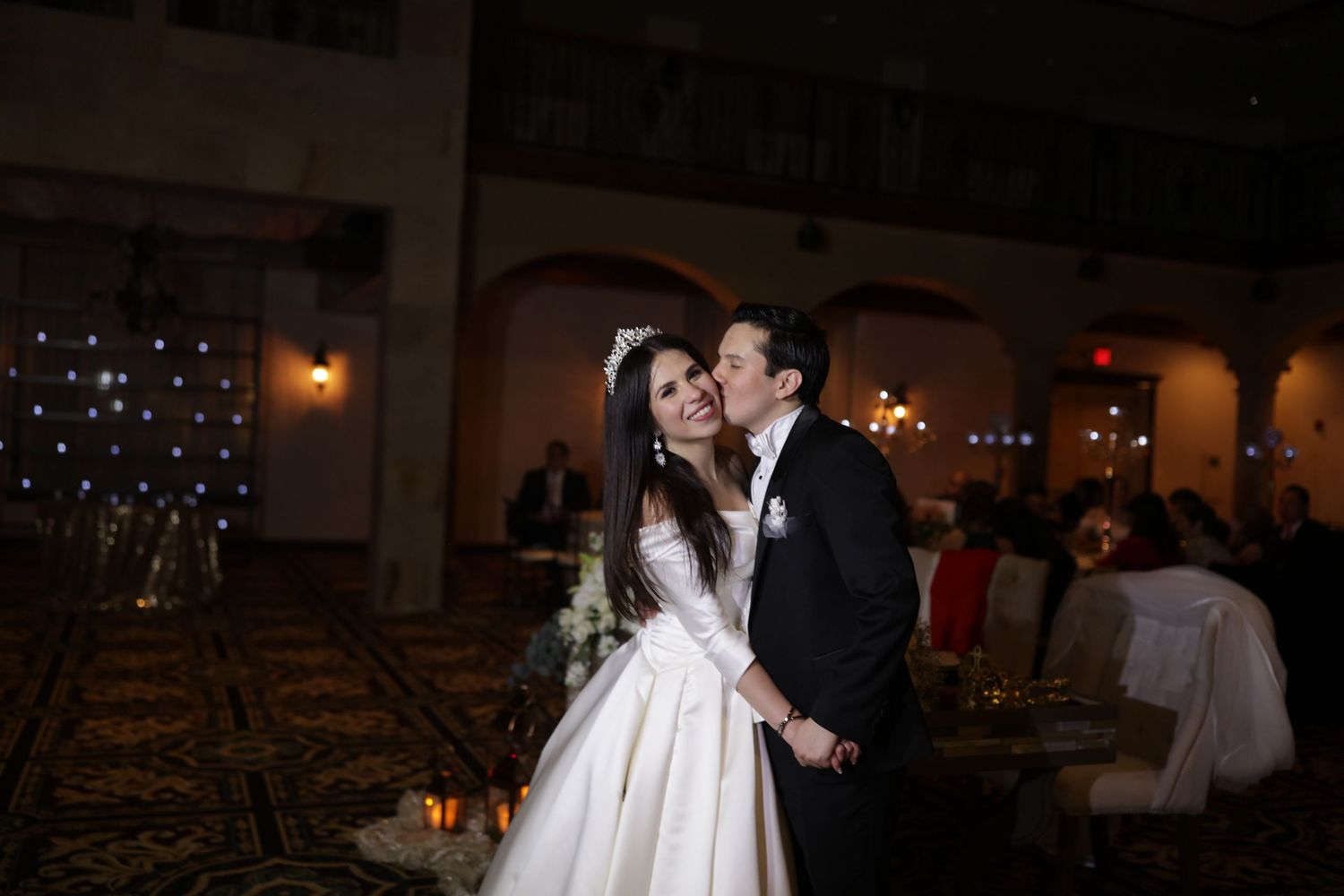 Bride and groom share a tender kiss on the dance floor during their elegant evening wedding reception.
