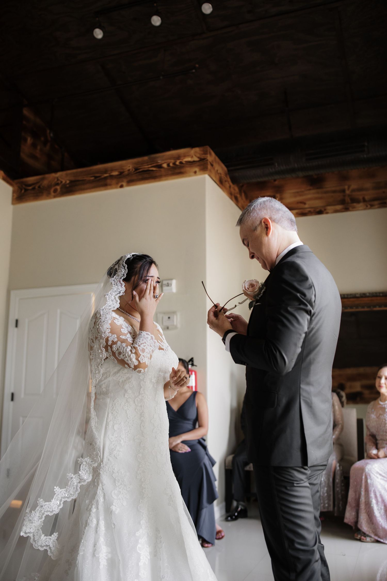 Emotional bride wipes tears as father presents rose during intimate wedding day first look moment.