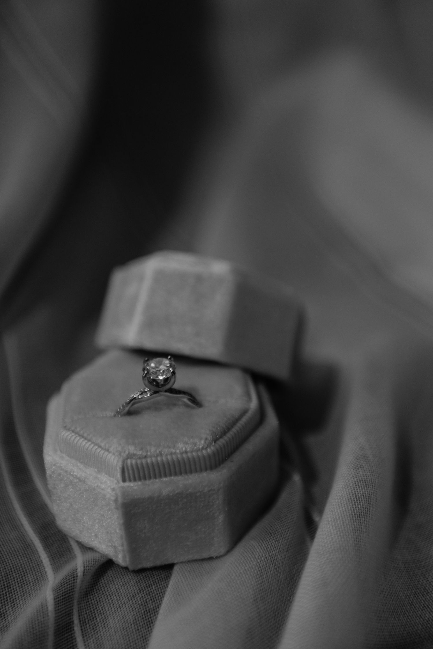 Black and white photo of a diamond solitaire engagement ring displayed in an octagonal velvet ring box.