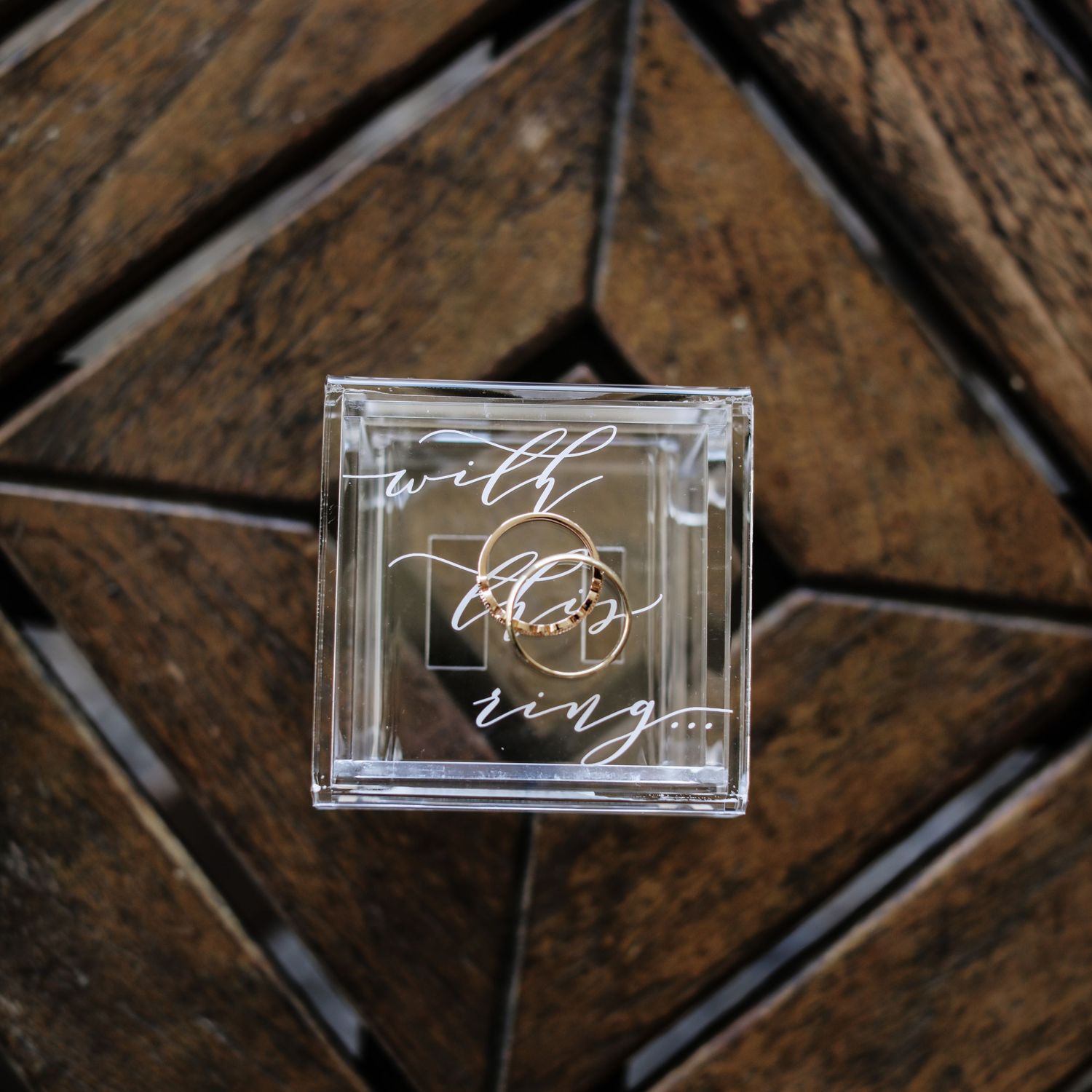 Clear acrylic wedding ring box with elegant calligraphy script on wooden background.