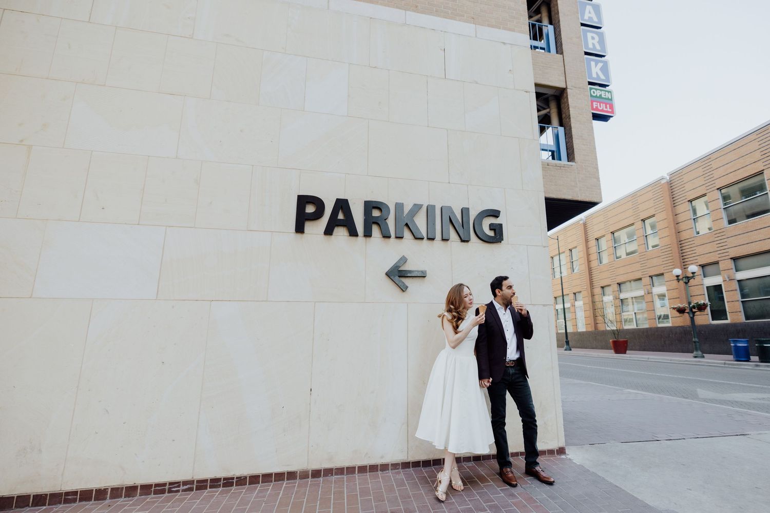 A stylish couple poses playfully next to a parking sign on a city wall.