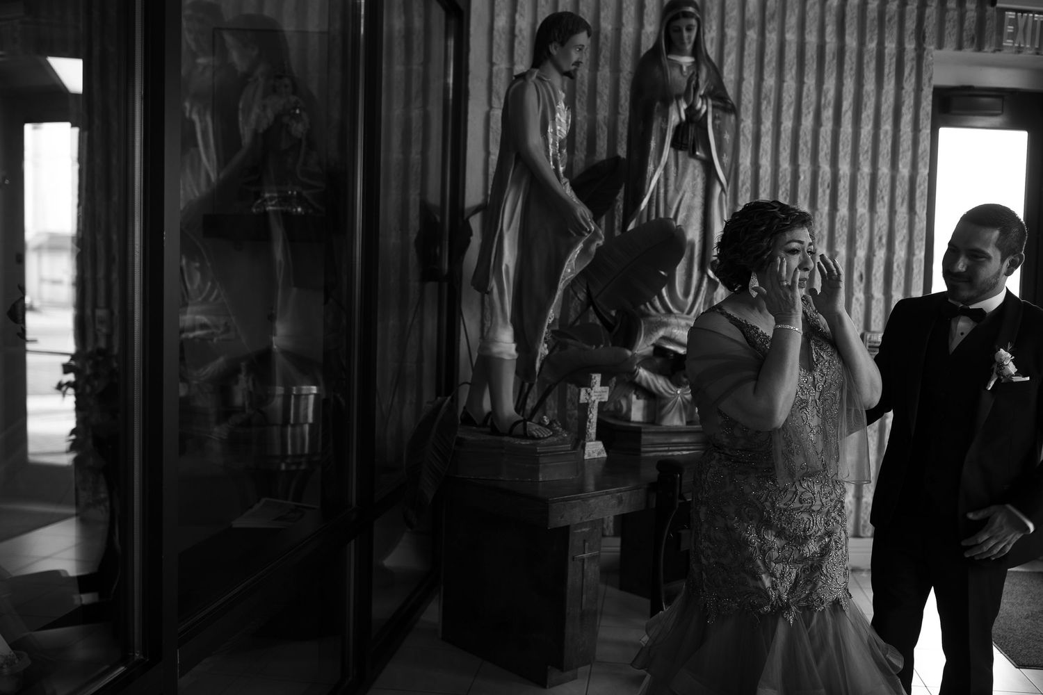 Emotional bride wipes tears near religious statues in a black and white wedding photo.