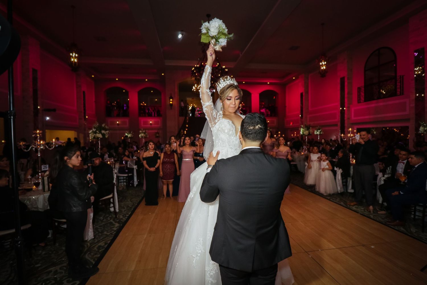 Bride raises bouquet triumphantly on the dance floor during wedding reception in an elegant ballroom.