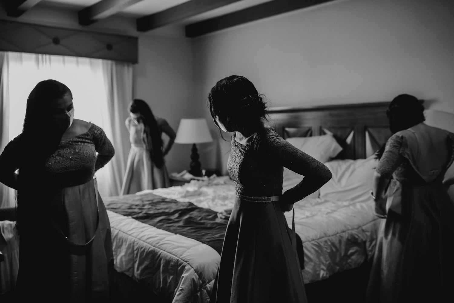 Bridesmaids helping each other get ready in a hotel room in black and white wedding photography.