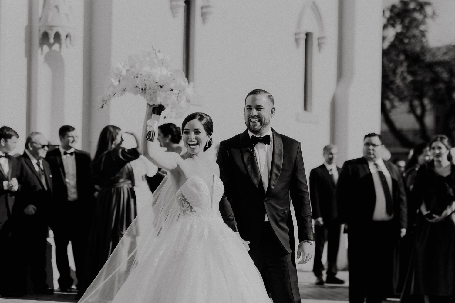 Wedding party stands outside white church columns in elegant black and white formal attire.