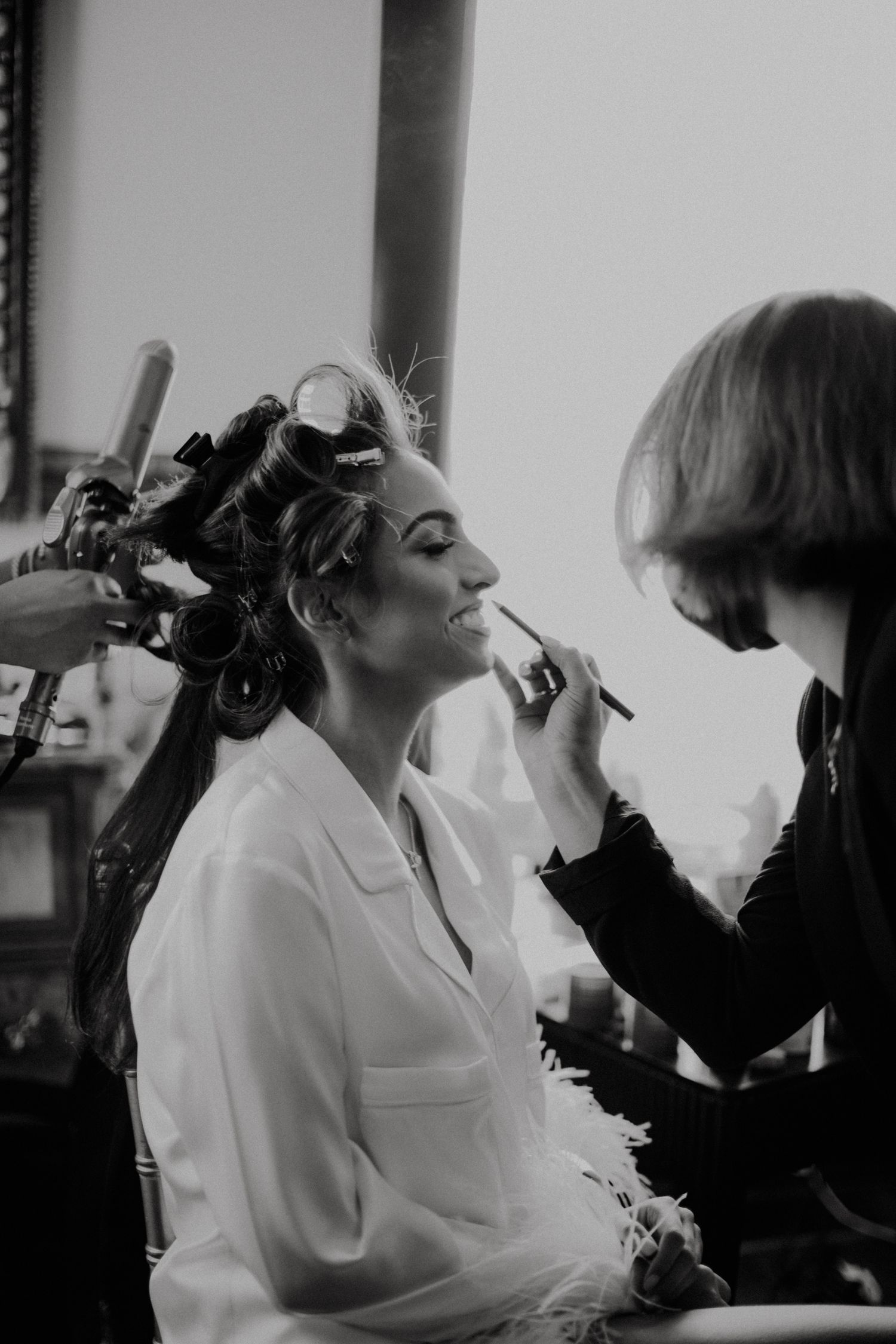 Black and white image of wedding preparations with makeup being applied to a bride.