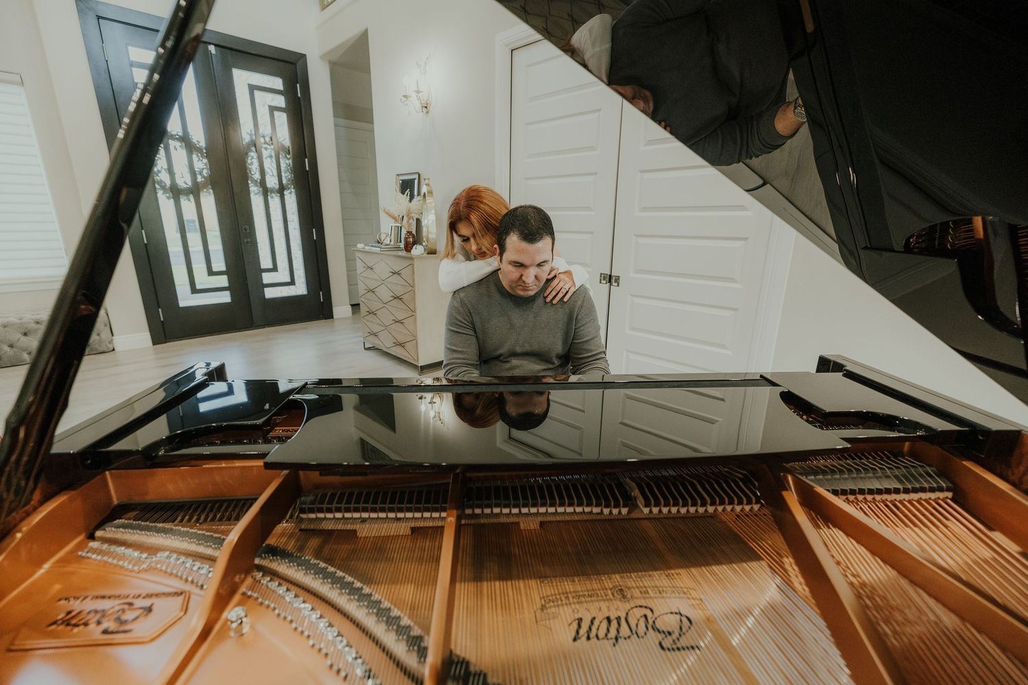 Man playing a grand piano while a woman watches in an elegant home interior setting.