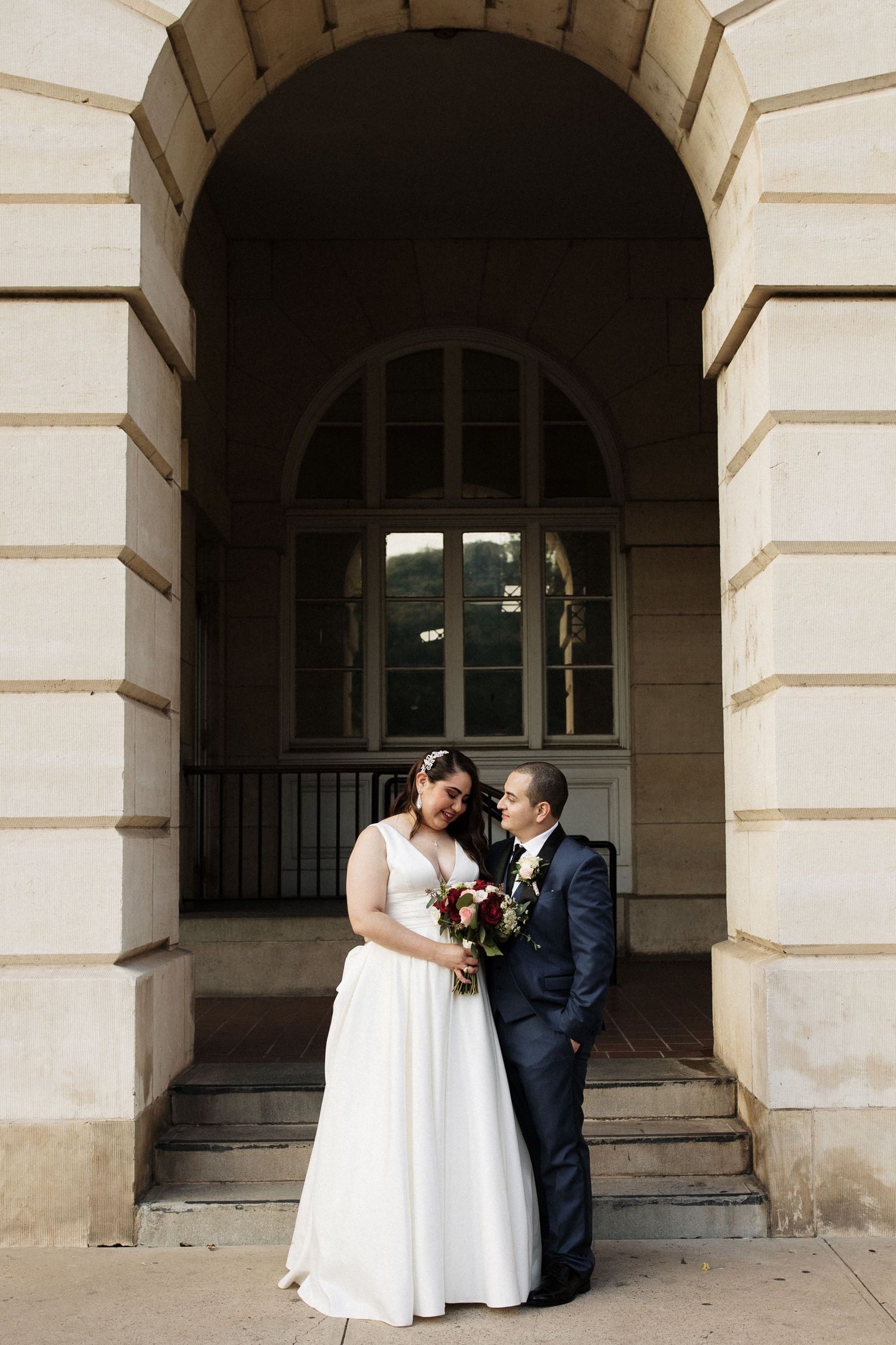 Bride and groom share intimate moment under stone archway at classic wedding venue.