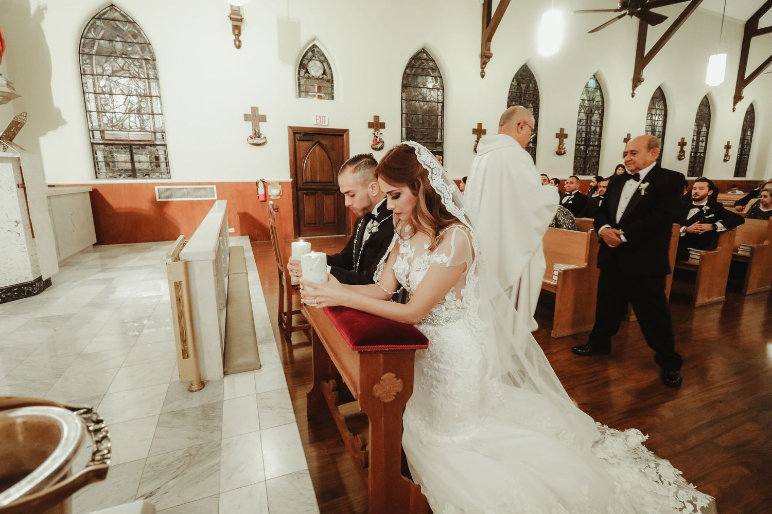 Bride and groom kneel together in prayer at ornate church altar during traditional wedding ceremony.