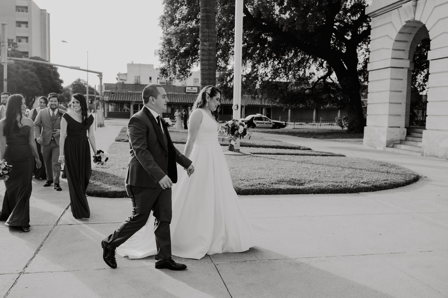 Black and white photo of bride and groom walking hand in hand outside a building on their wedding day.