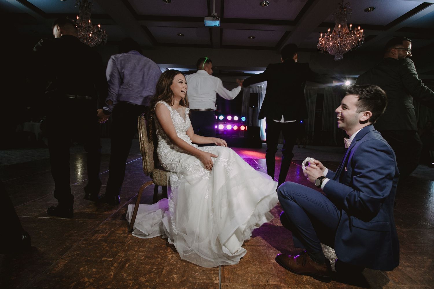 Groom kneeling before bride during the garter removal tradition on the wedding dance floor.