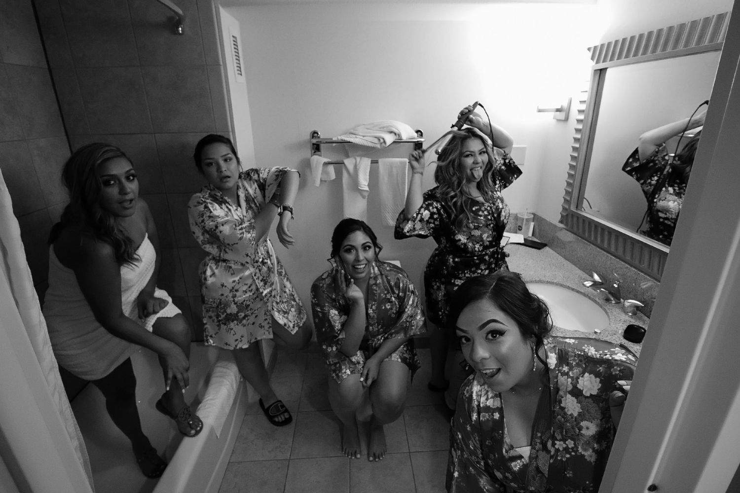 Black and white photo of bridesmaids getting ready together in hotel bathroom before wedding ceremony.