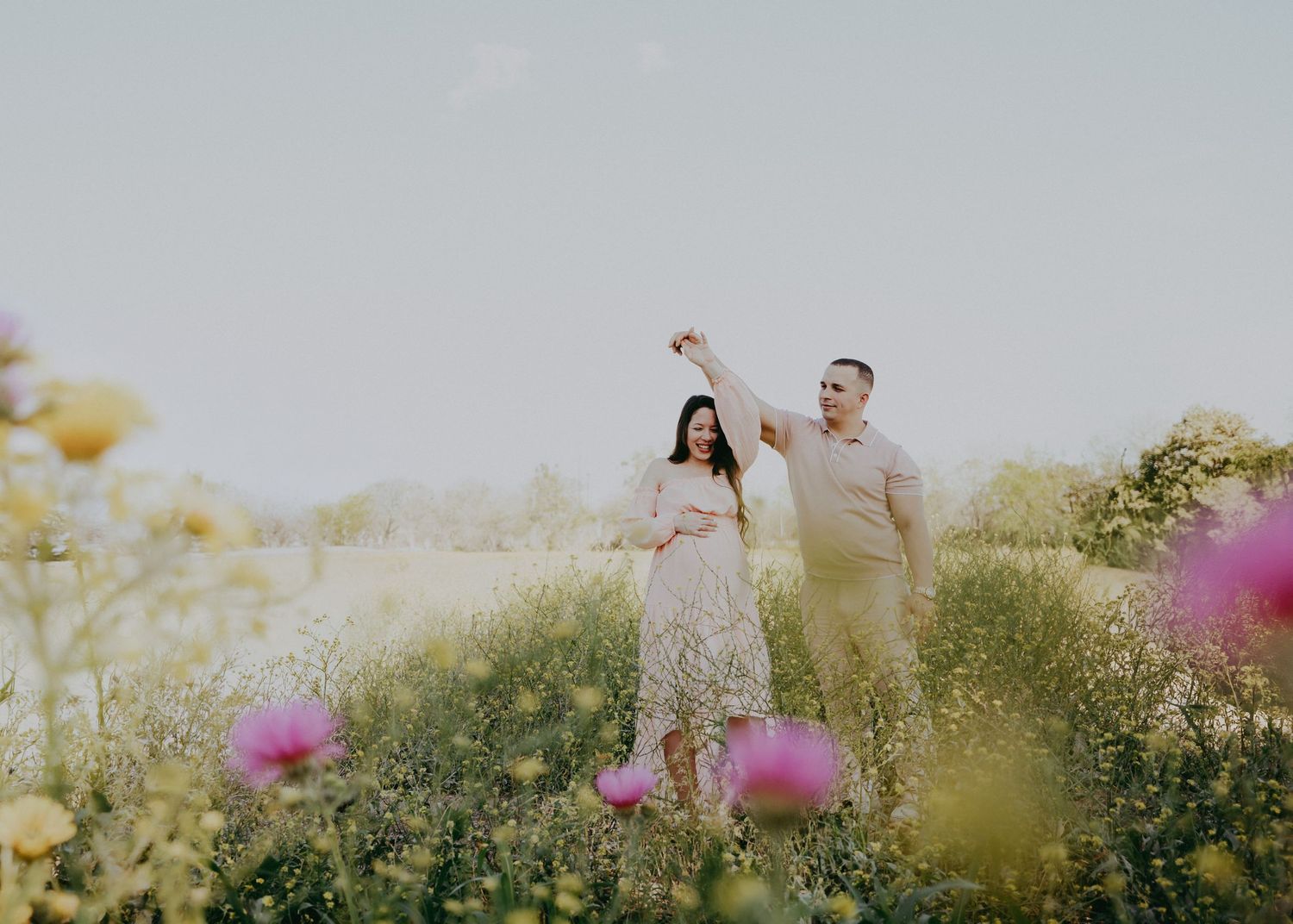 A couple stands in a dreamy meadow filled with wildflowers during a romantic outdoor photoshoot at golden hour.