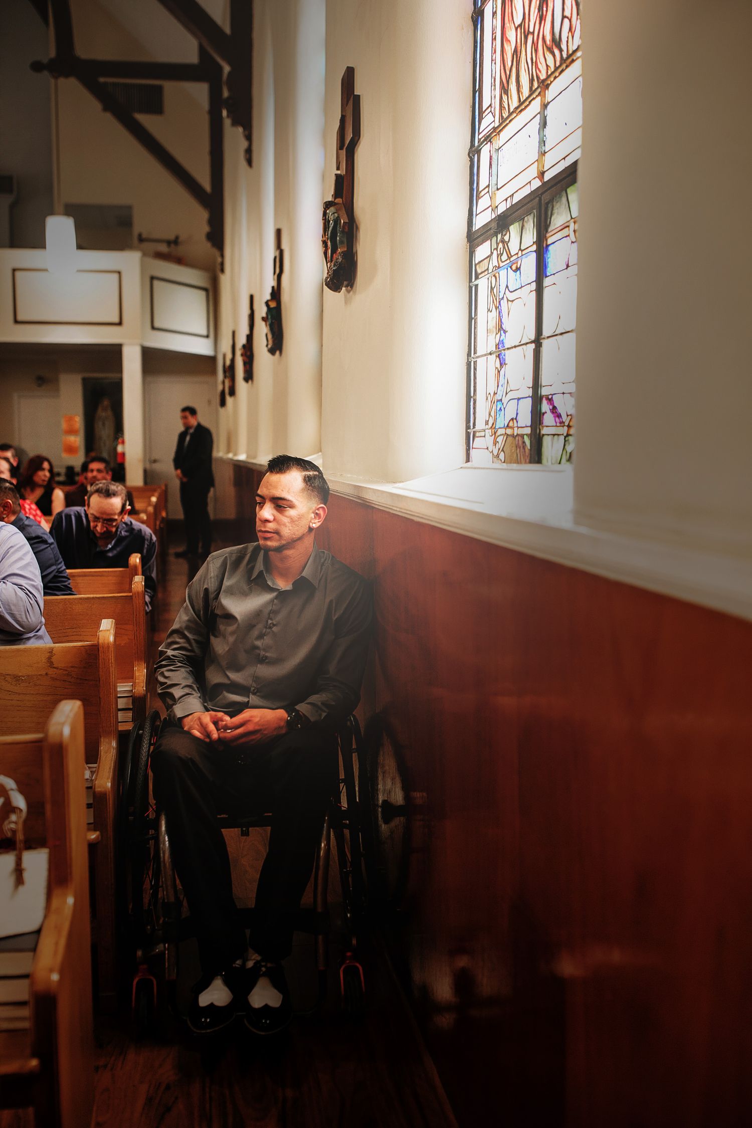 Man in wheelchair sitting in church pew beside stained glass window at wedding.