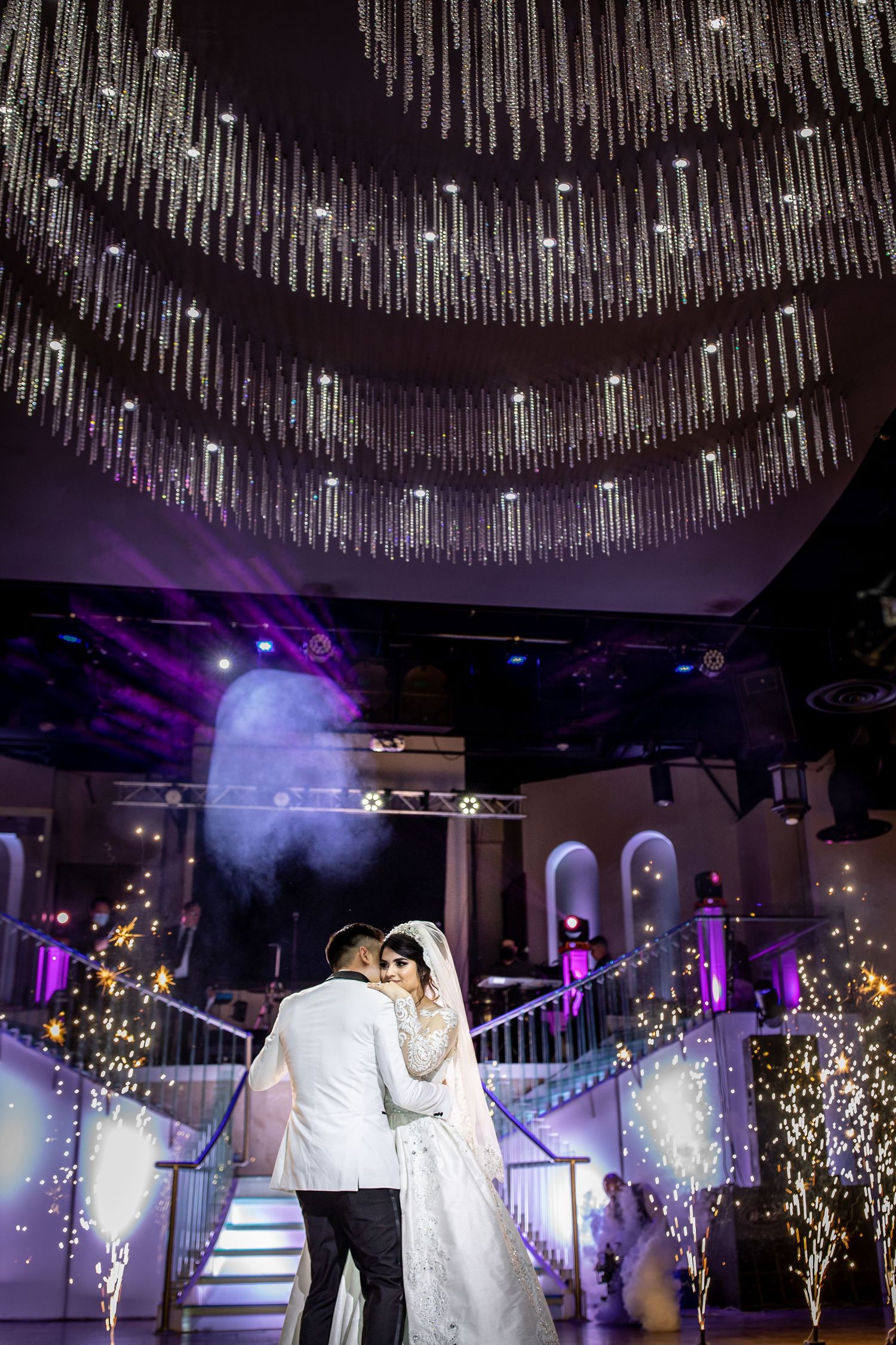 Bride and groom share first dance under sparkling crystal chandelier with fireworks.
