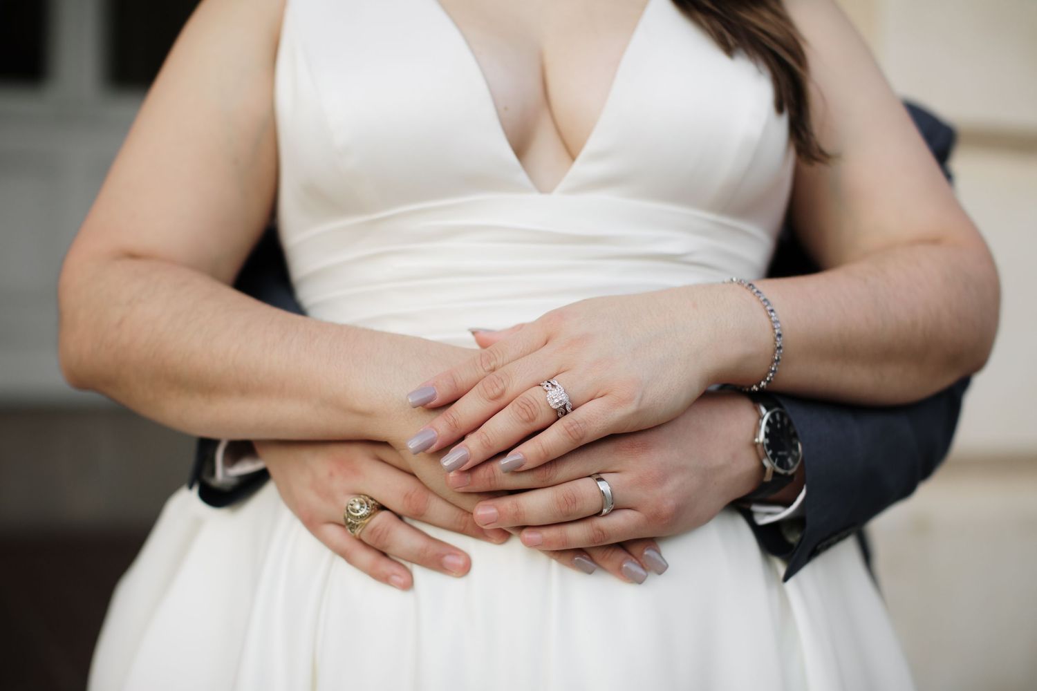 A close-up of a bride and groom holding hands showing their wedding and engagement rings.