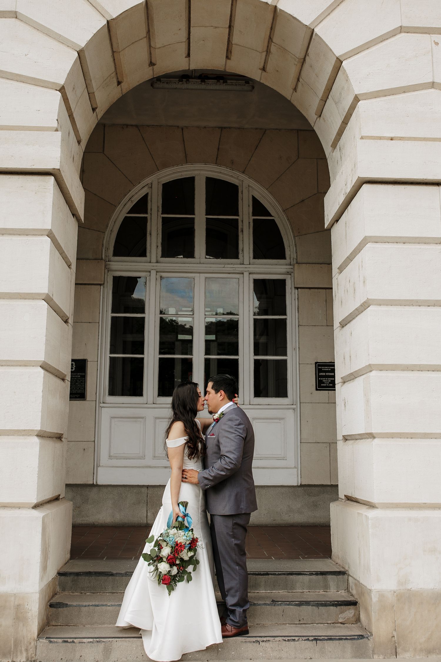 Bride and groom sharing a kiss under arched doorway of classic building.