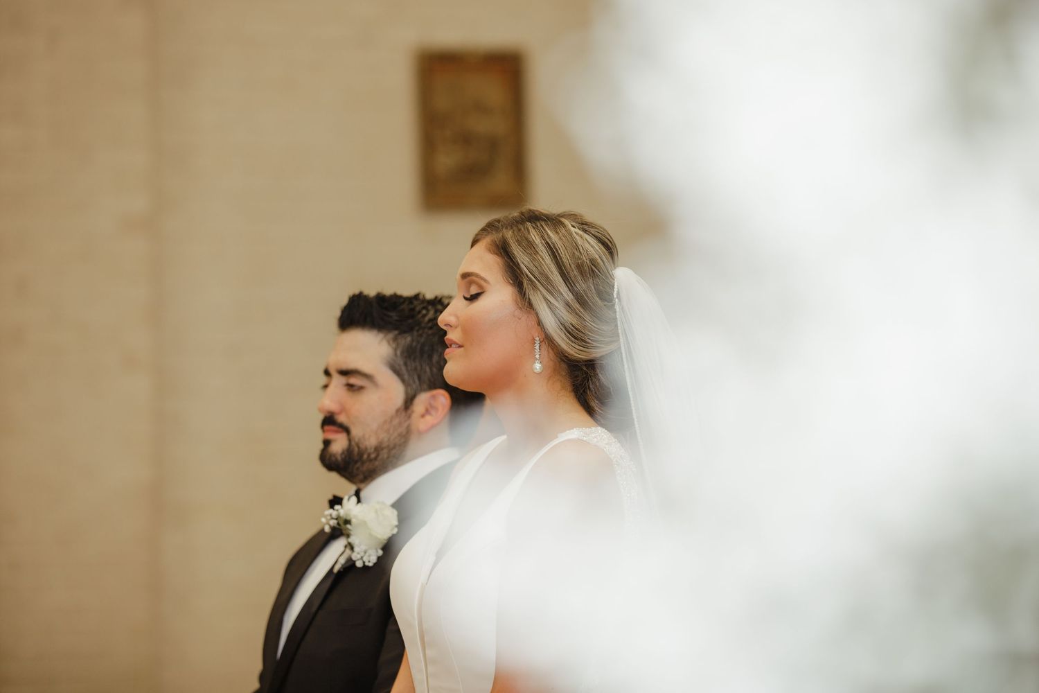 Bride and groom stand together during their wedding ceremony, bride wearing a flowing veil.