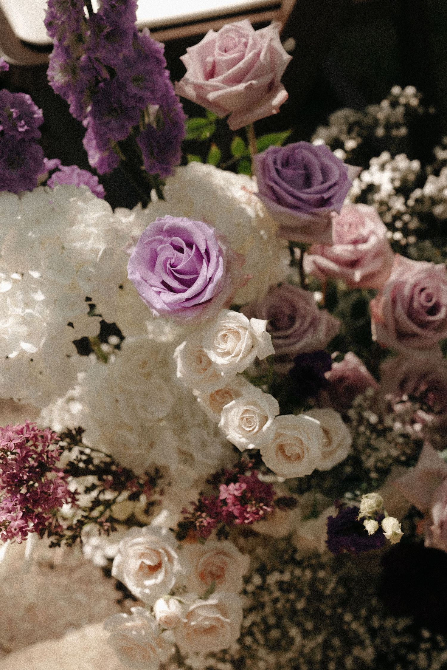 Elegant floral arrangement featuring purple and pink roses with white blooms against a dark background.