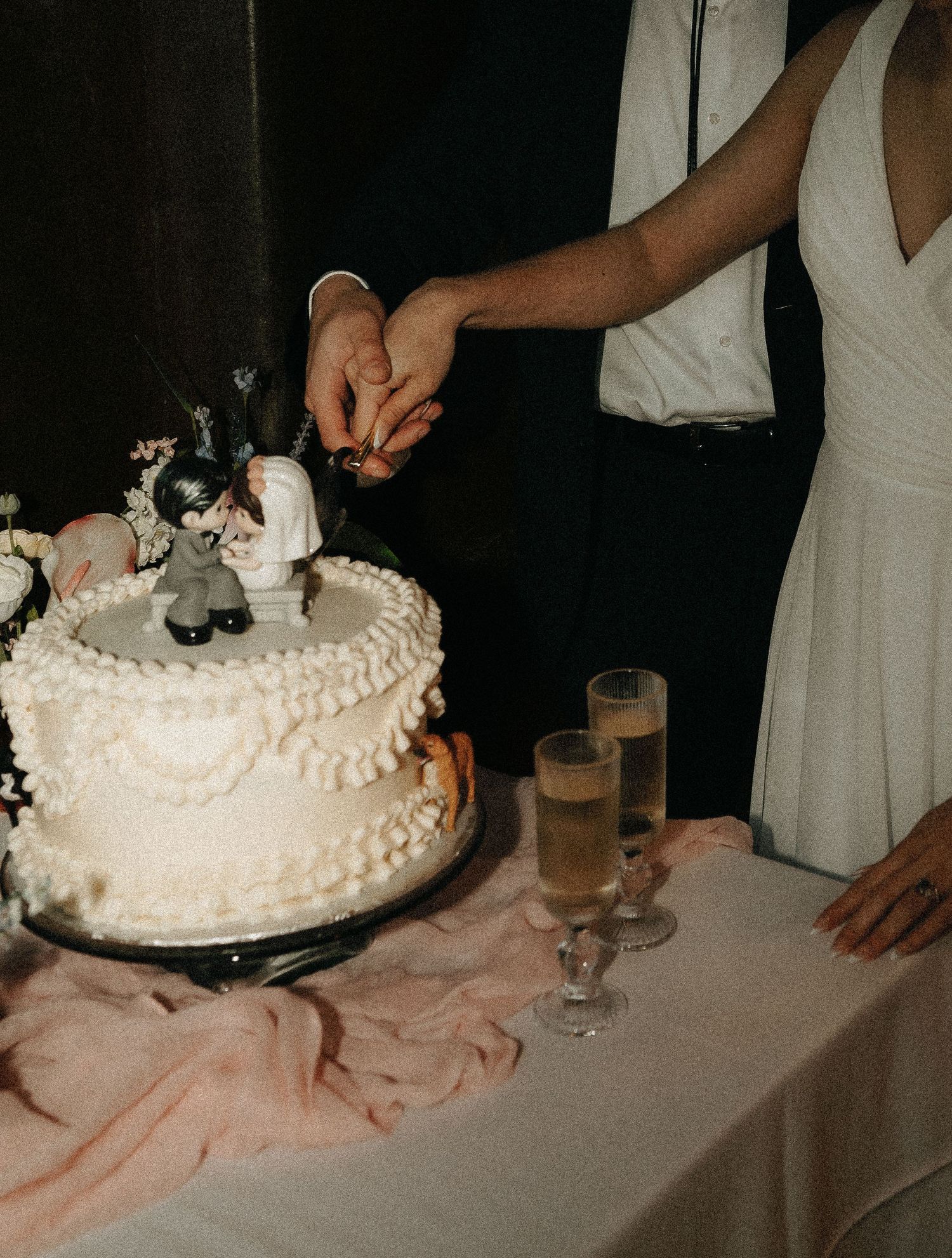 White wedding cake being cut on a table with pink tablecloth.