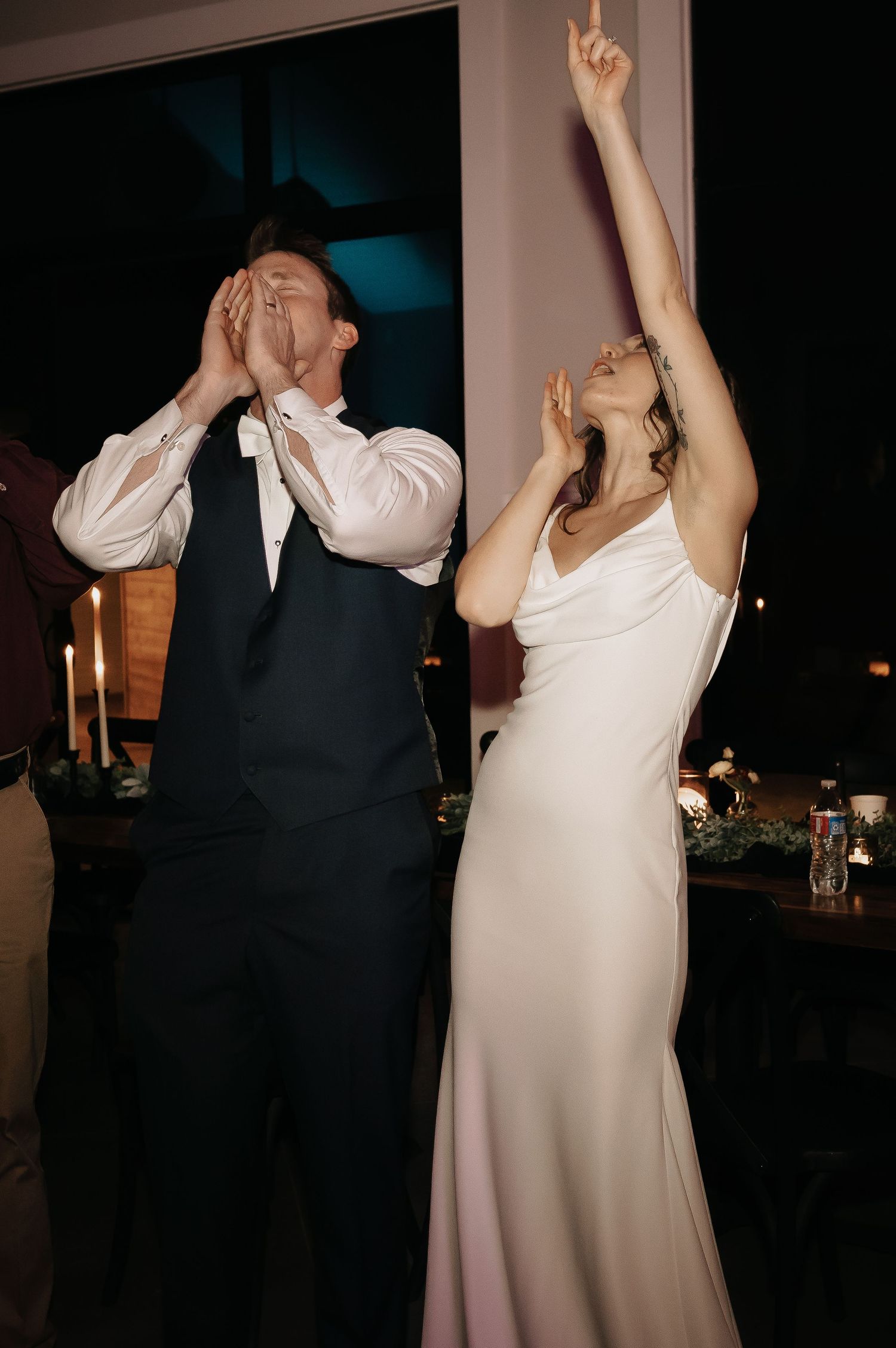 Wedding guests dancing and celebrating with raised arms on a dark dance floor.
