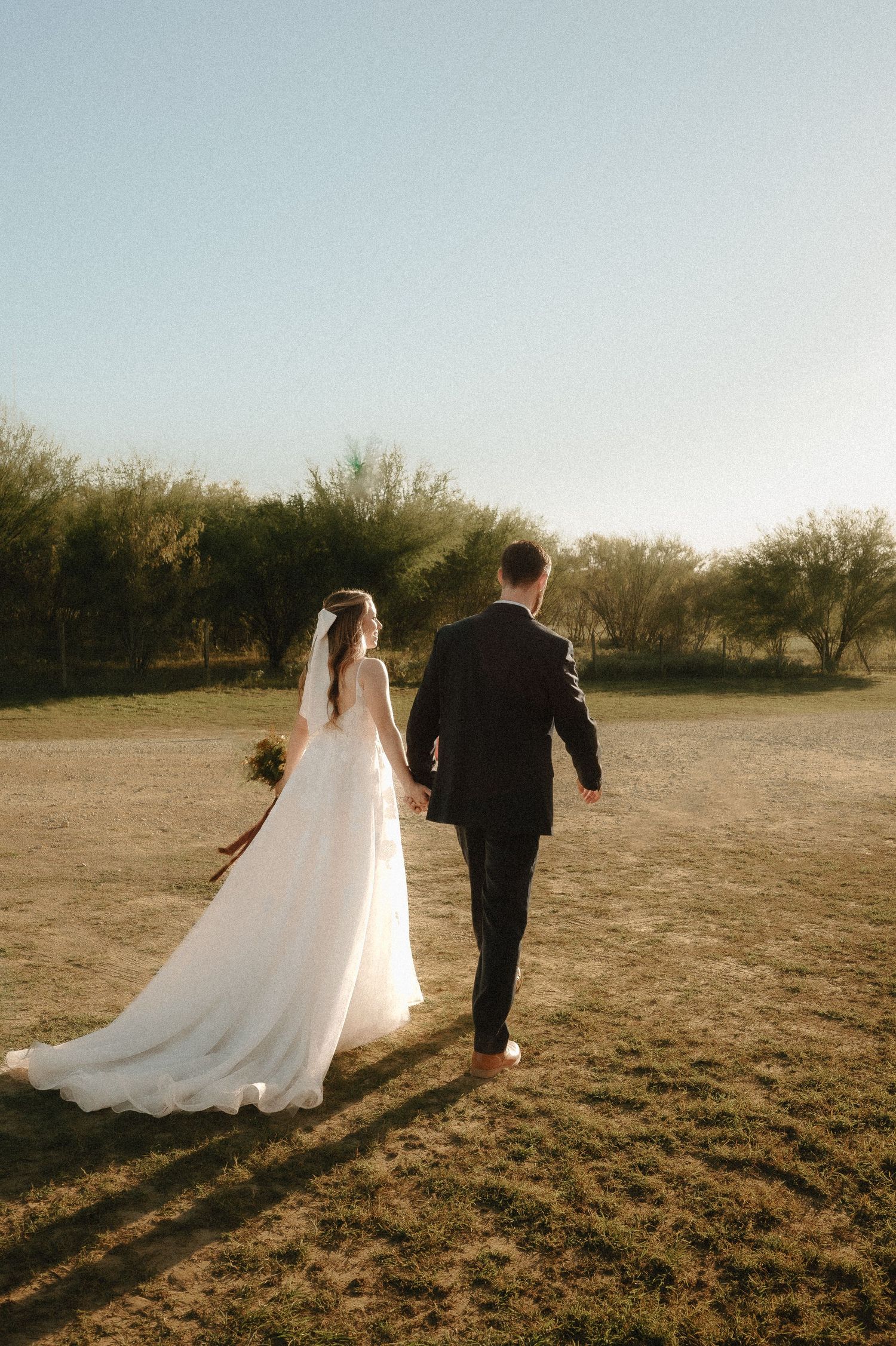 Sunset silhouette of newlyweds walking together across an open field.