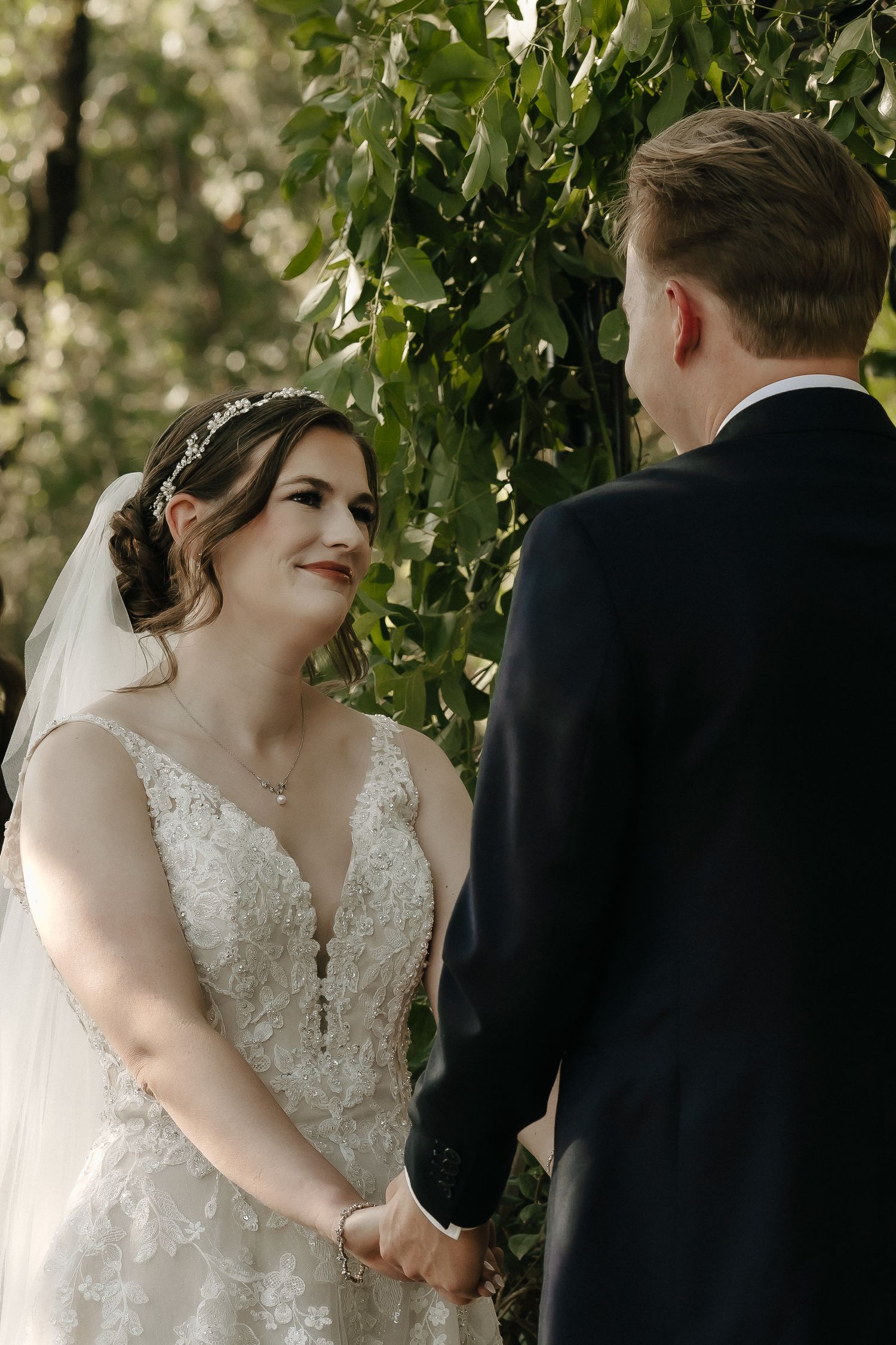 Wedding ceremony exchange between couple under green foliage outdoors.