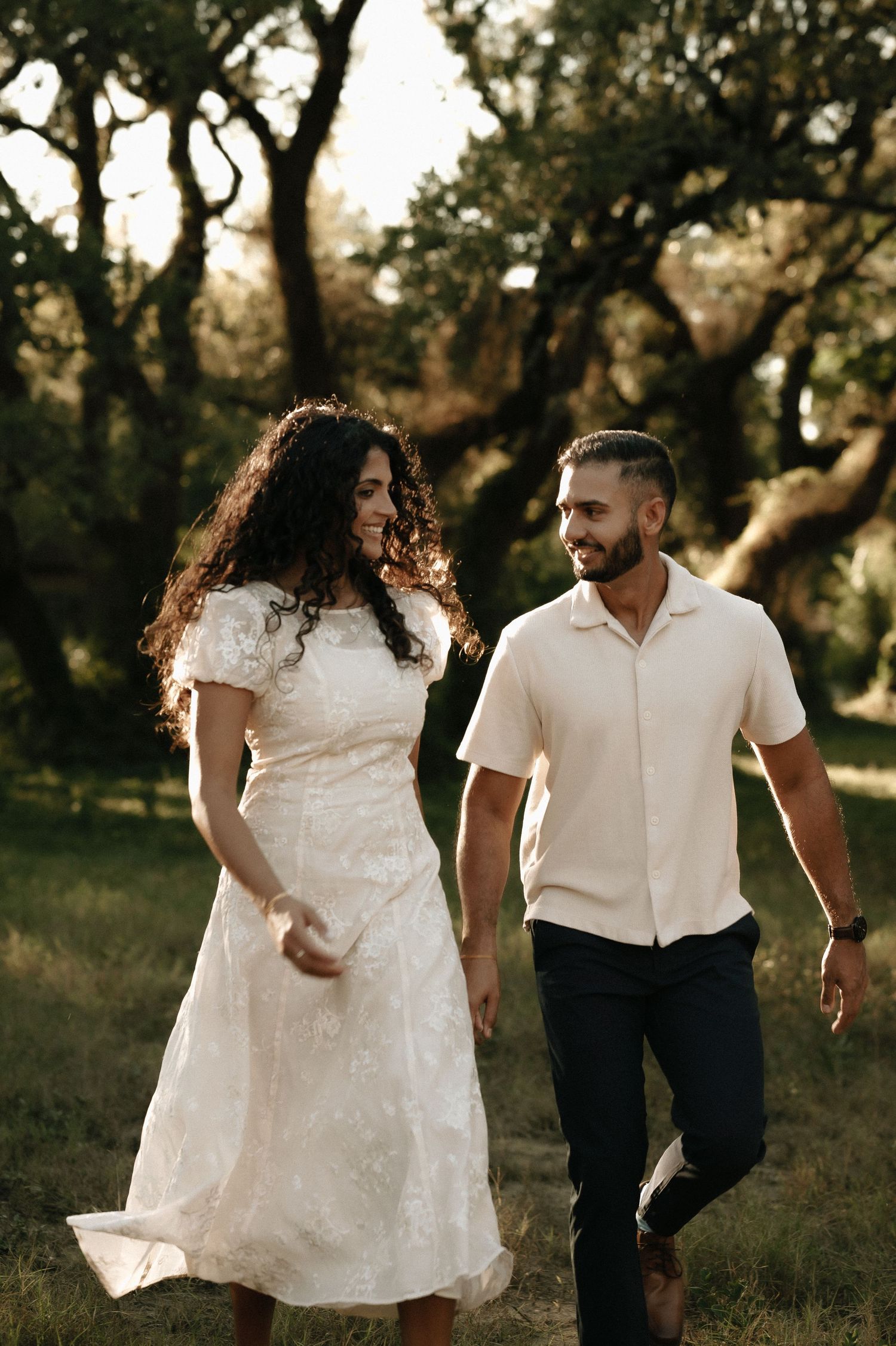 Couple walking together through a scenic park in coordinated white outfits.