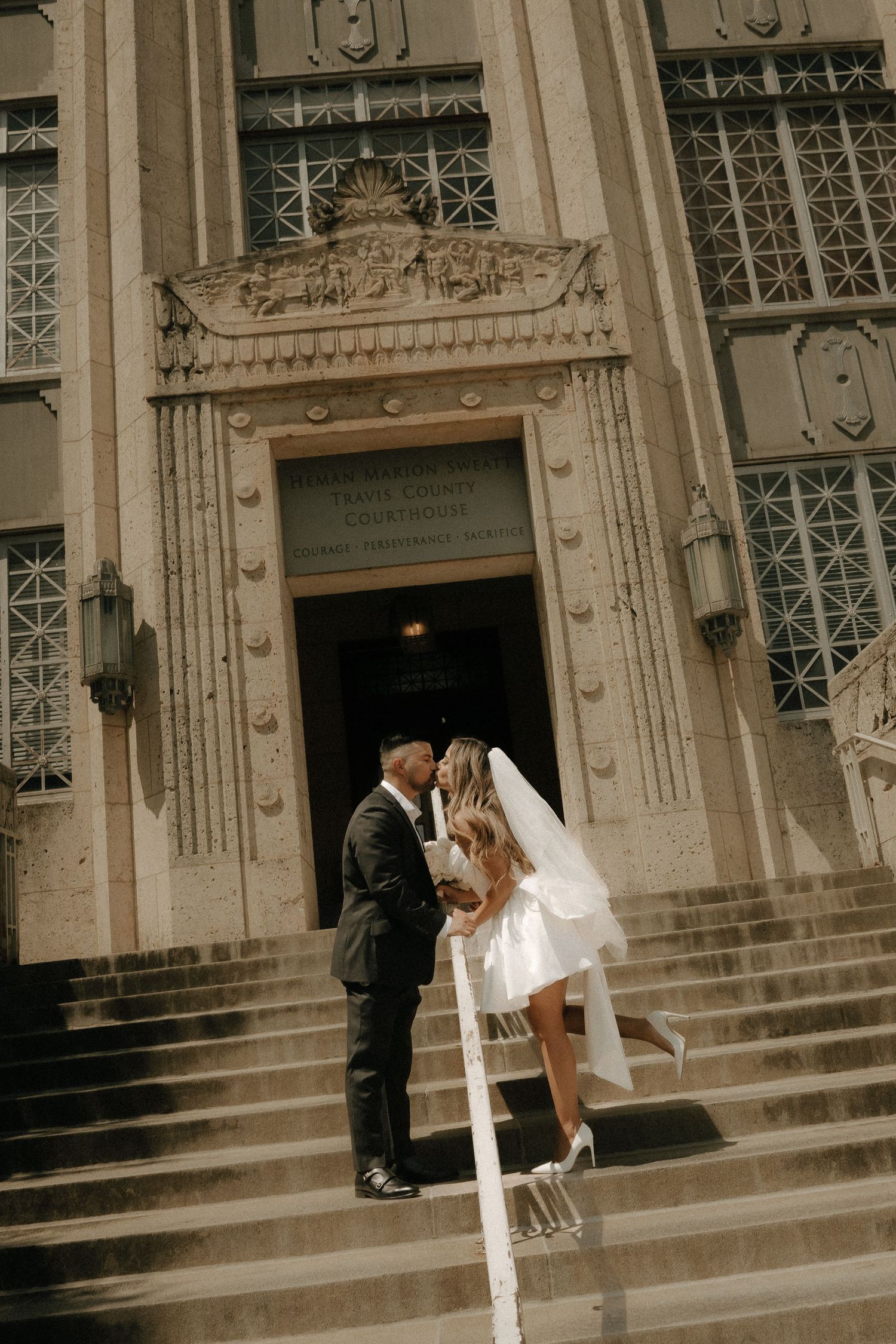 A couple shares a tender moment on grand stone steps of a historic building.