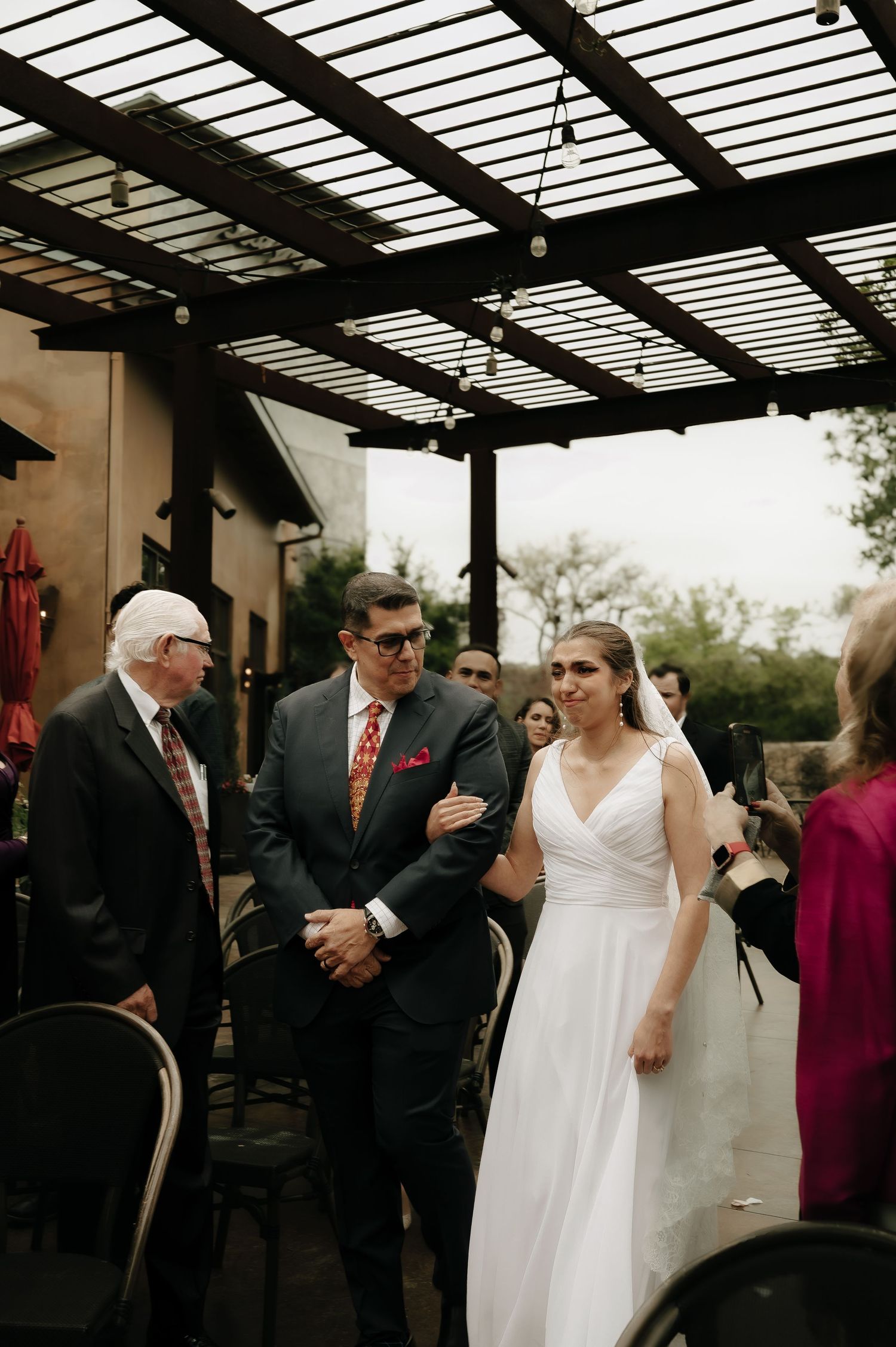 Wedding celebration under a slatted pergola with natural lighting.