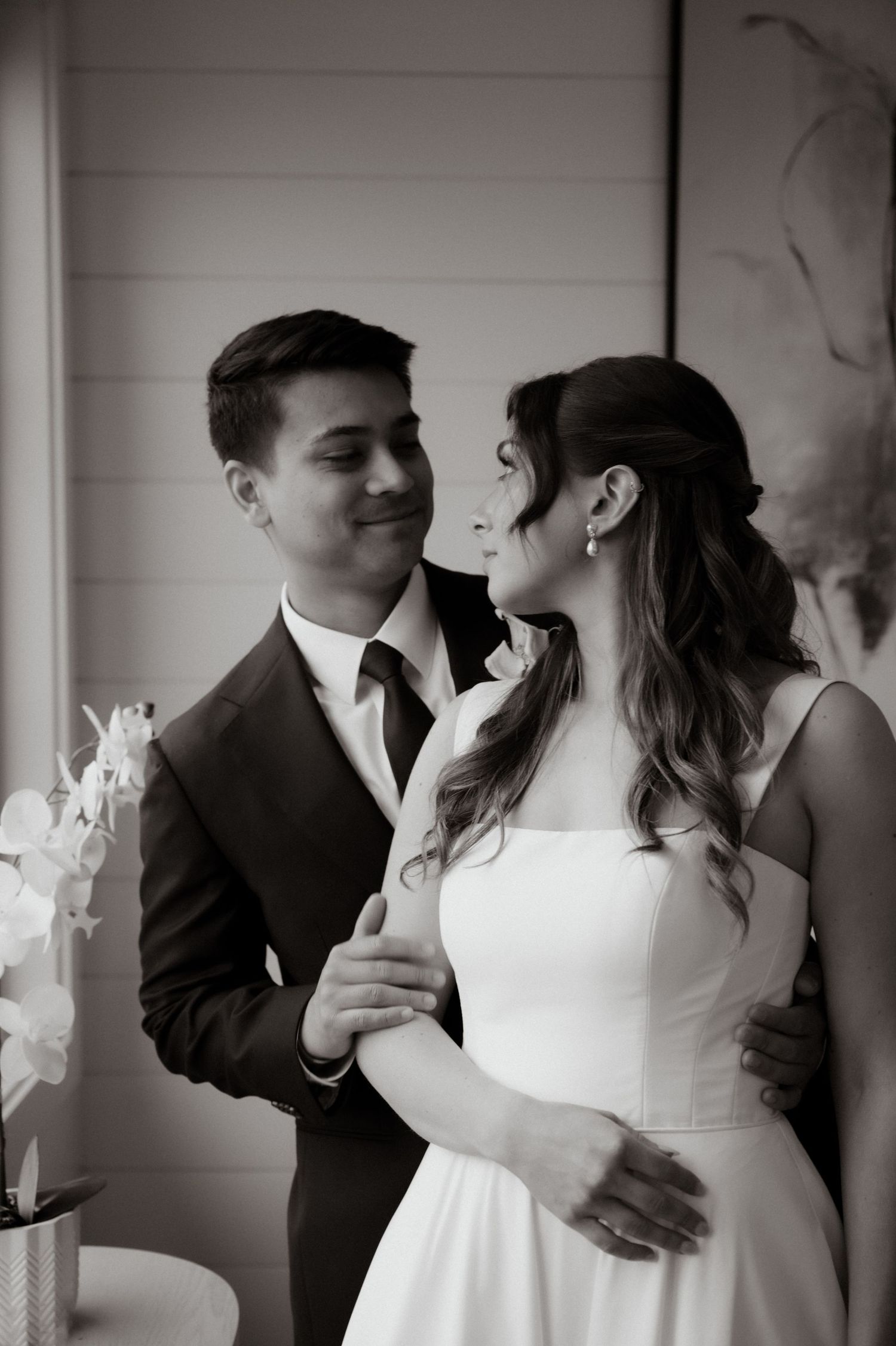 Black and white photo of a couple in wedding attire sharing a tender moment, groom in suit, bride in white dress.