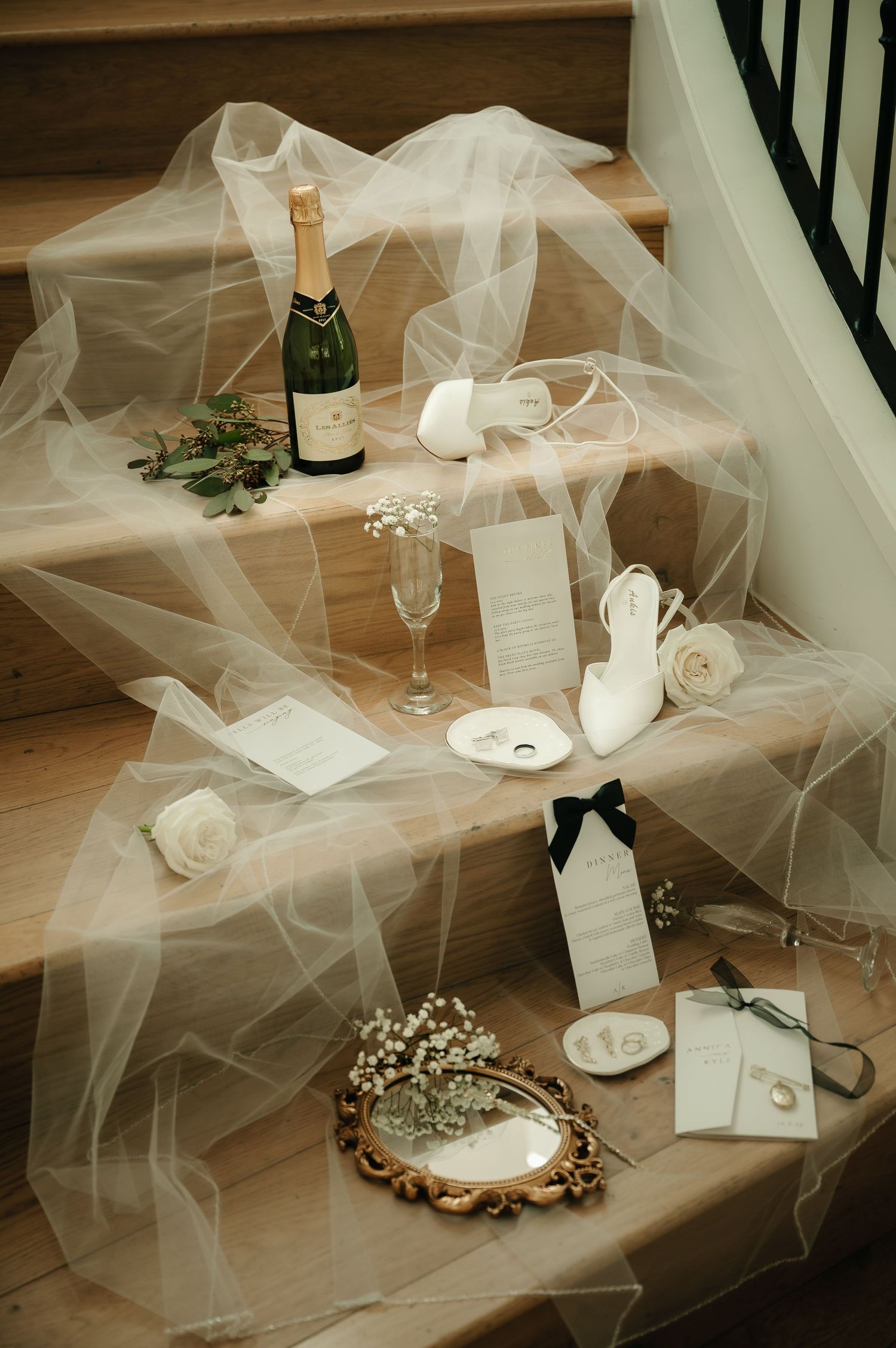 Wedding accessories arranged on wooden steps with flowing tulle fabric and champagne glasses.