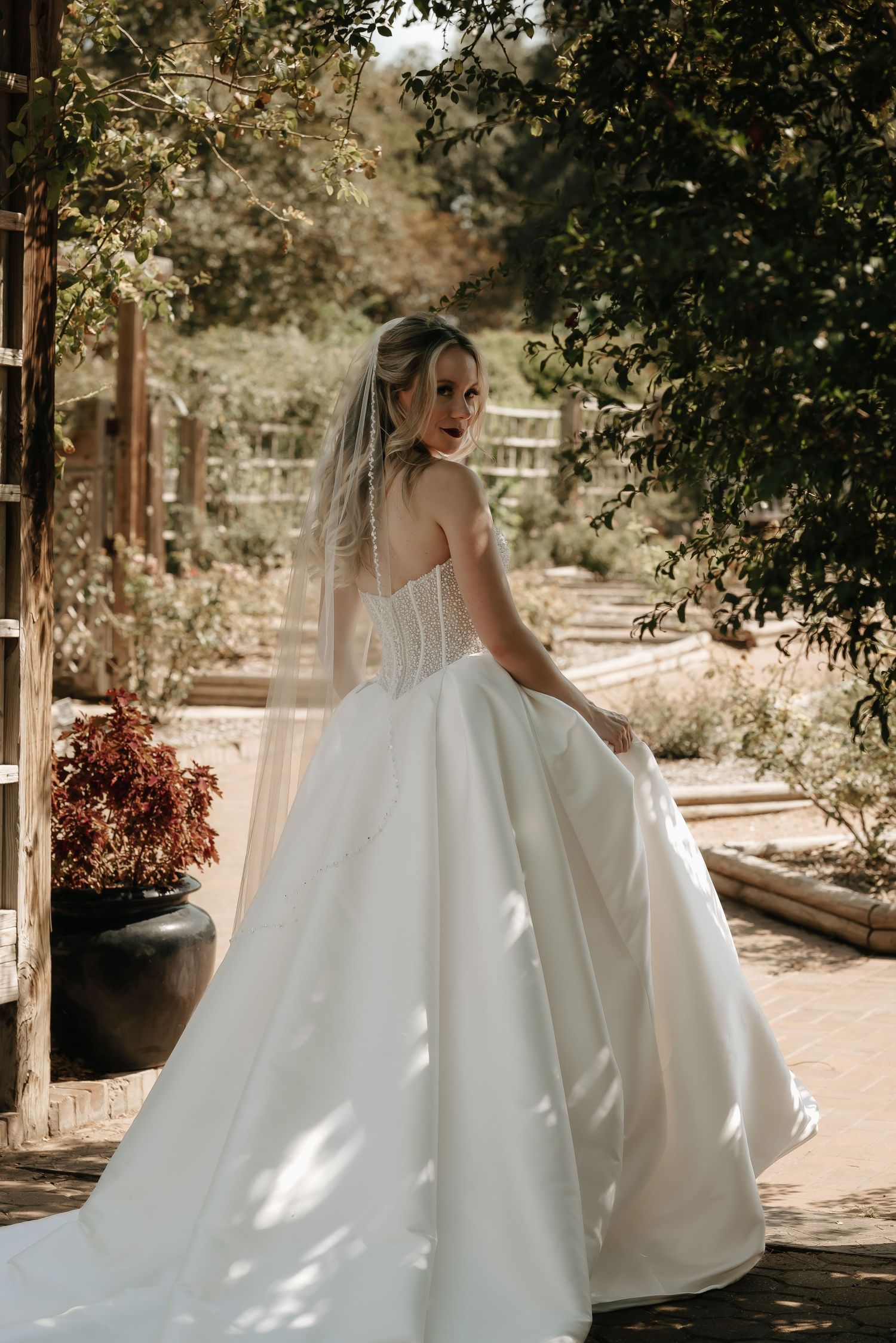 Elegant bride in a white ballgown poses in a garden setting with natural light.